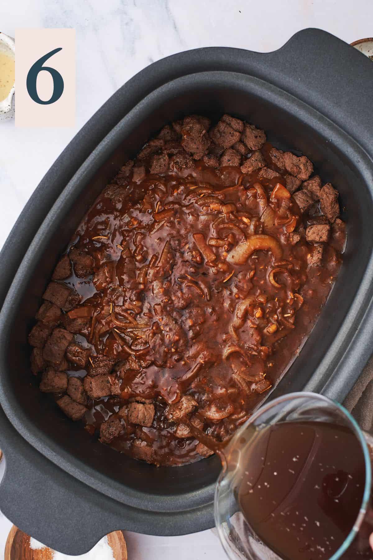 pouring beef stock into a slock cooker with cooked beef, onions, and garlic.