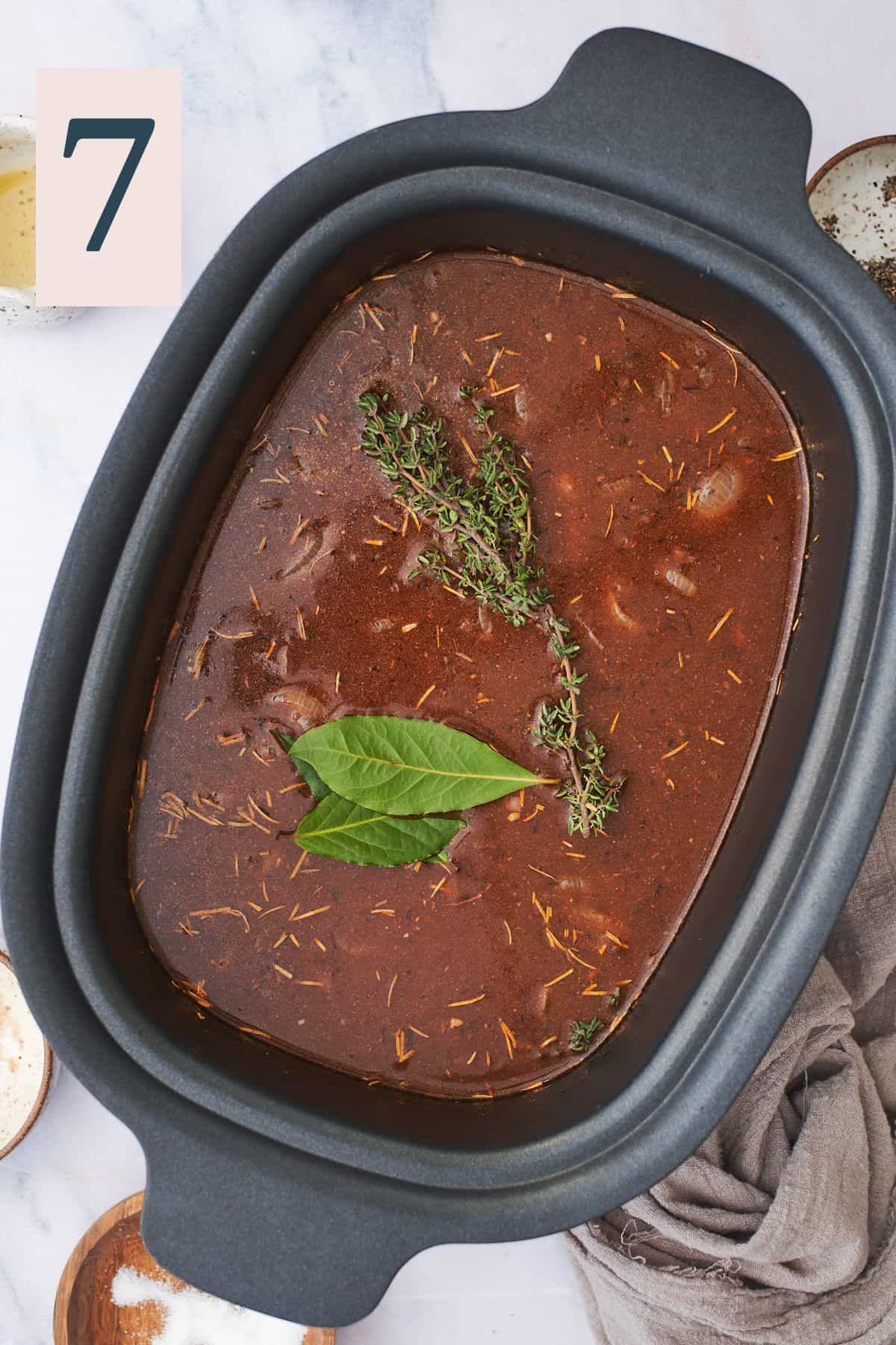 beef stew in a slow cooker topped with bay leaves, and thyme. 