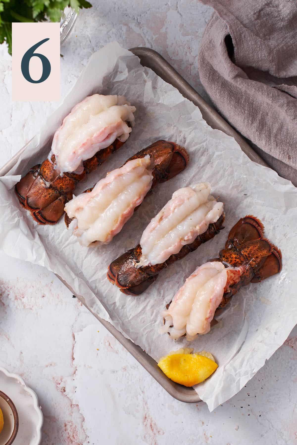 lobster tails spread overtop of the shells on a parchment lined baking sheet.