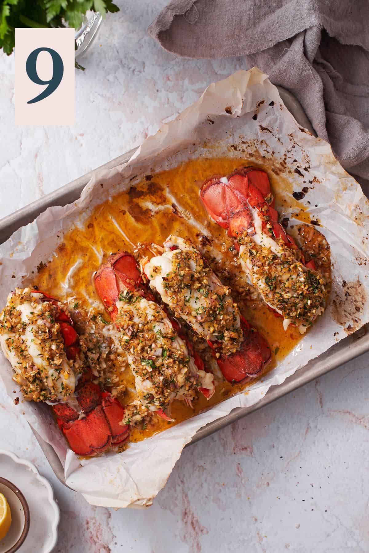 cooked lobster tails with a buttery garlic herb and shallot mixture on a parchment lined baking sheet.