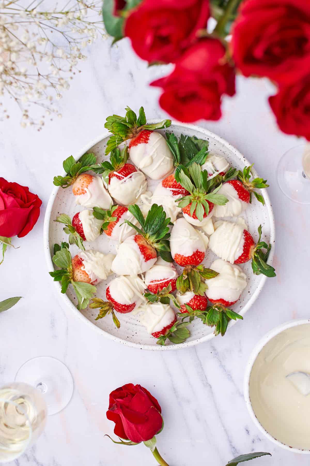overhead shot of white chocolate covered strawberries, red roses, and sparkling wine. 