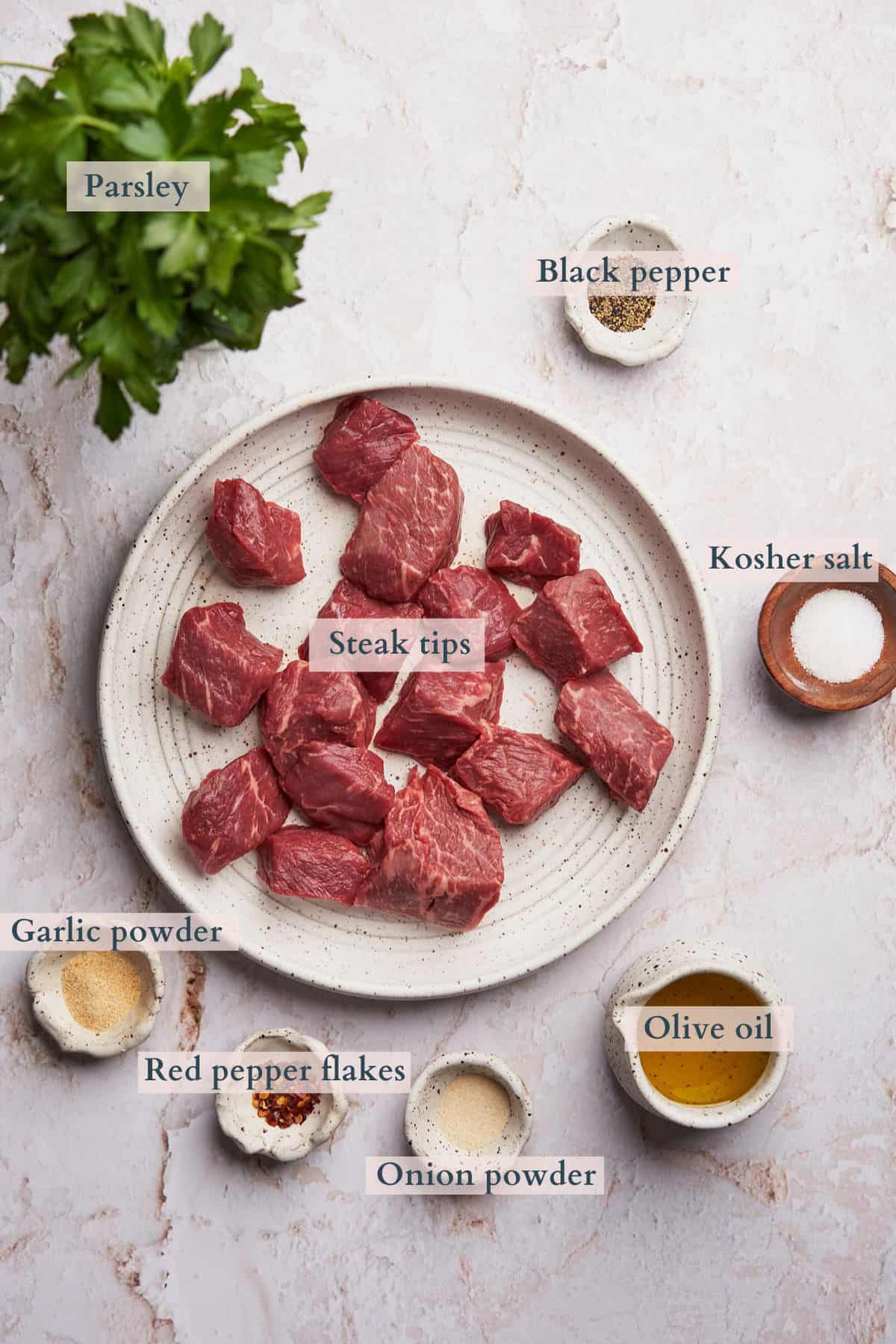 Ingredients for air fryer steak tips displayed in various containers and plates.