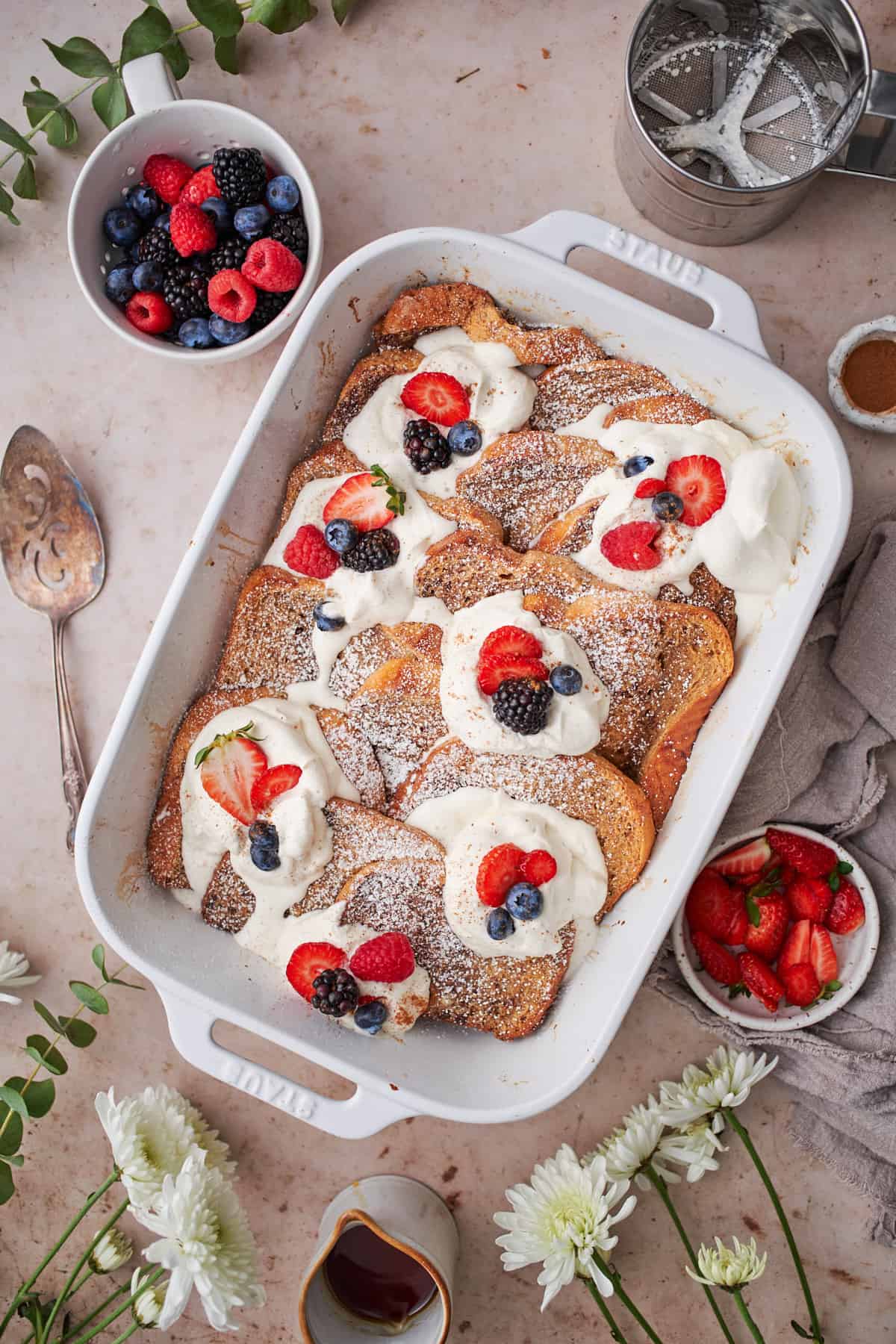 flat lay overhead of a brioche french toast casserole in a rectangular baking dish, topped with whipped cream and fresh fruit.
