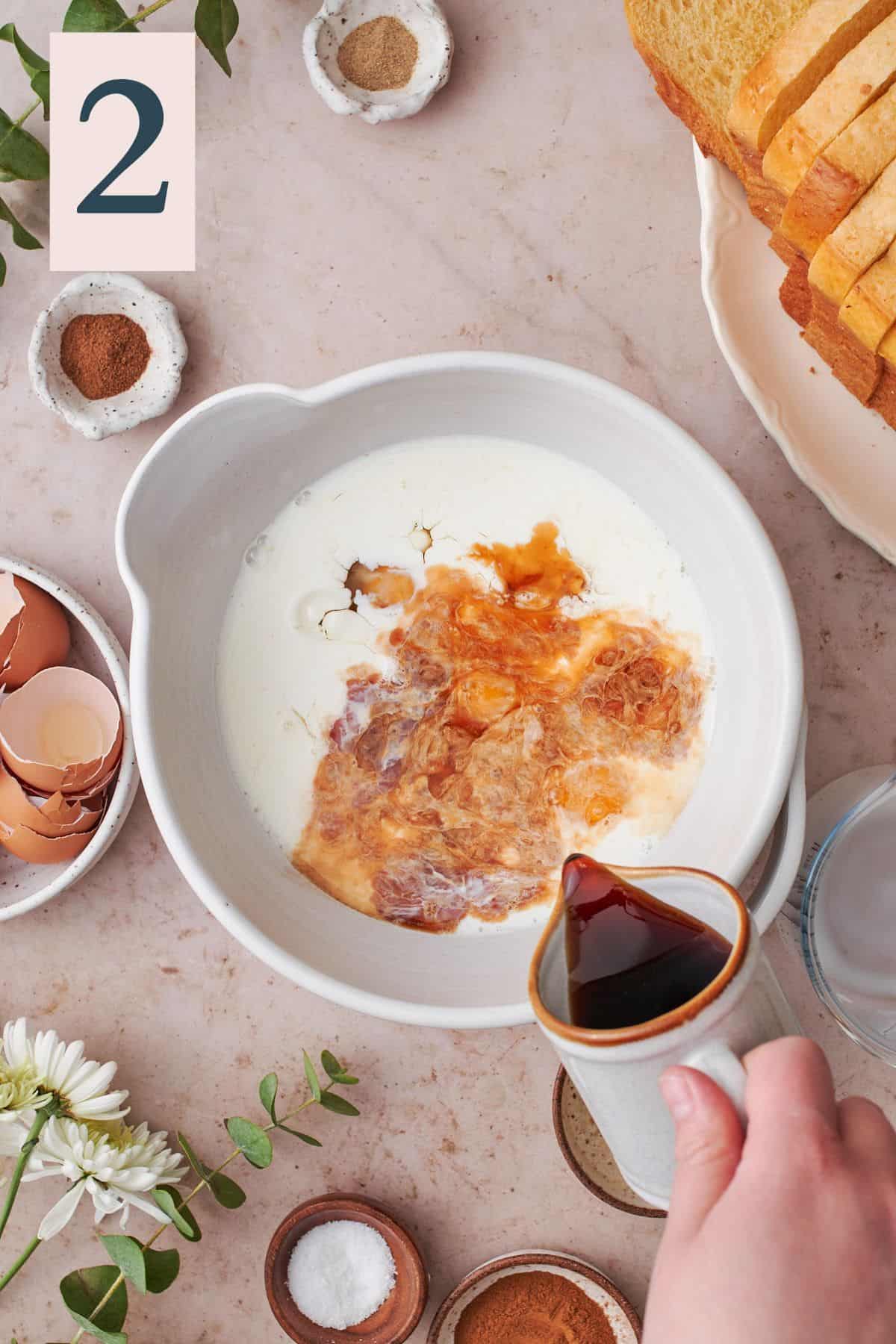 milk, eggs, and vanilla in a large bowl, with a hand pouring maple syrup into the bowl. 
