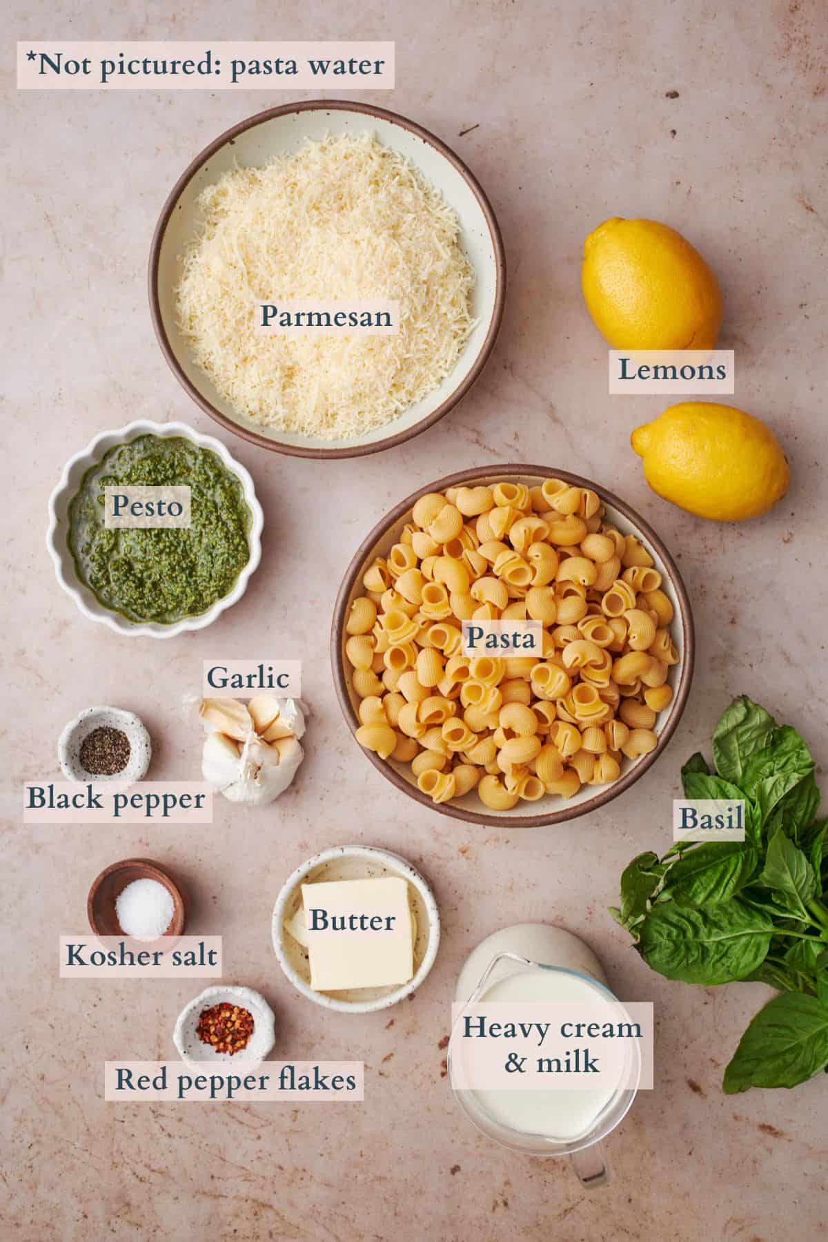 ingredients to make creamy pesto pasta laid out in bowls and labeled to denote each ingredient.