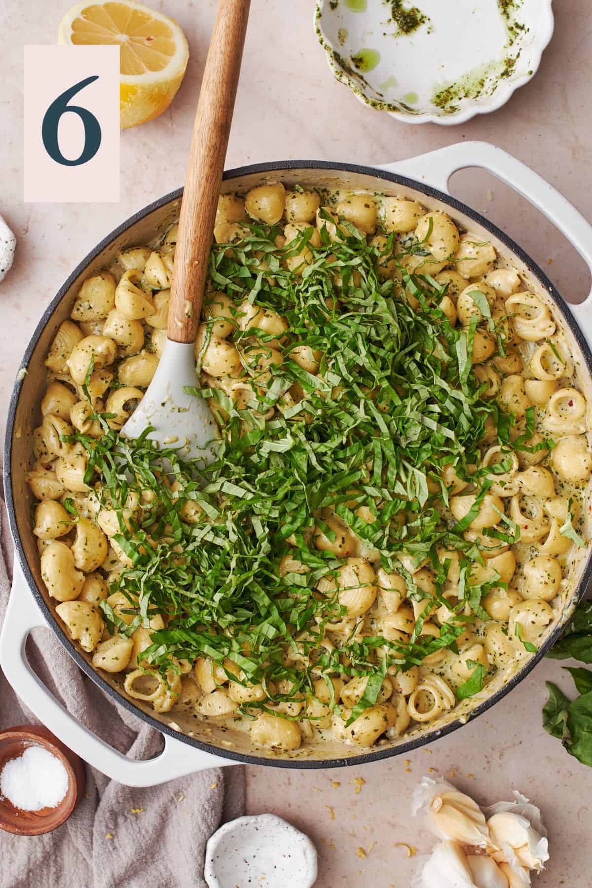 basil ribbons added to a skillet full of cooked pasta. 