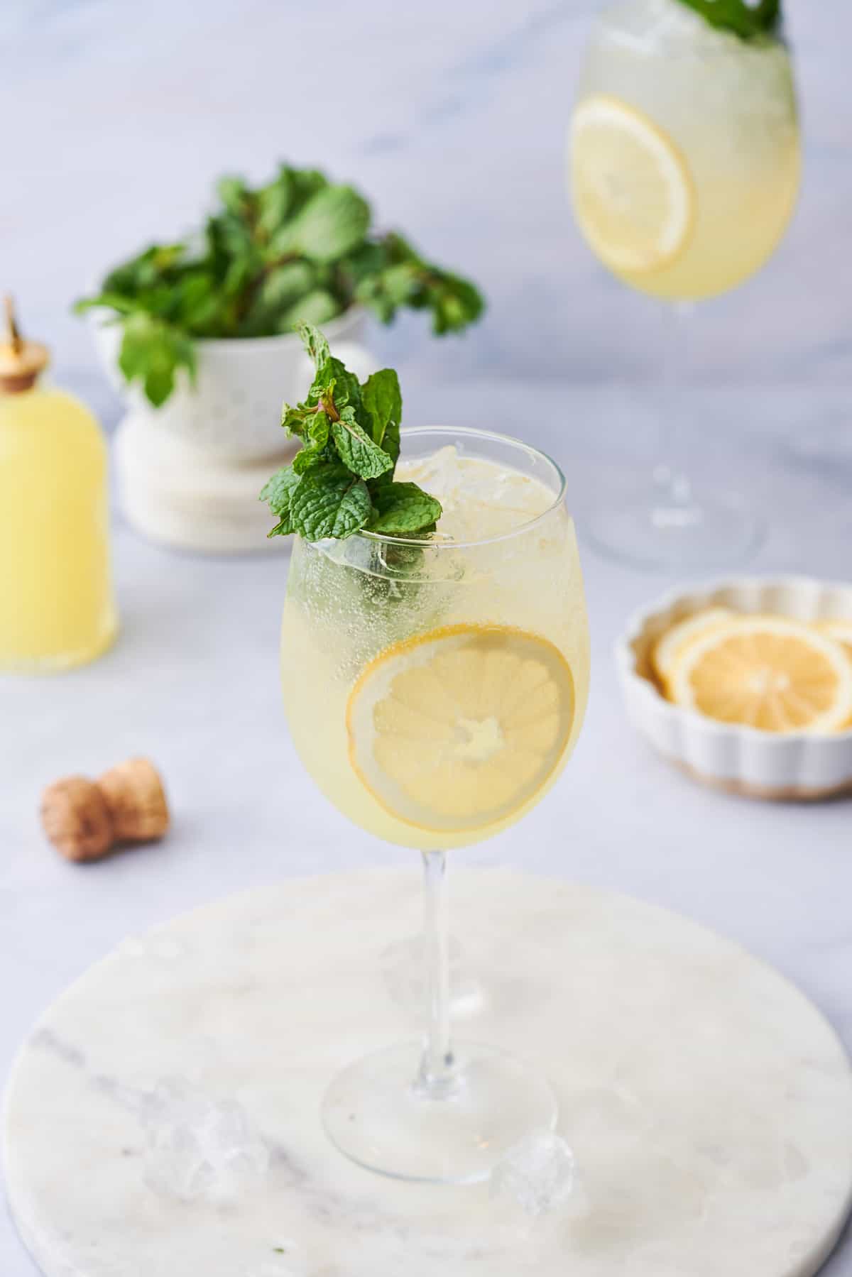 stunning photo of a pale yellow limoncello spritz with fresh lemon rounds and mint sprigs. 