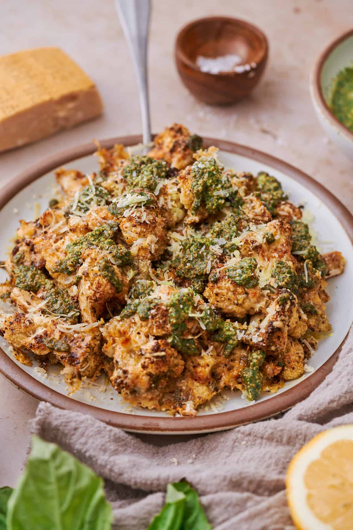 crispy parmesan pesto cauliflower on a plate topped with fresh walnut pesto, and grated parmesan cheese on a ceramic plate. 