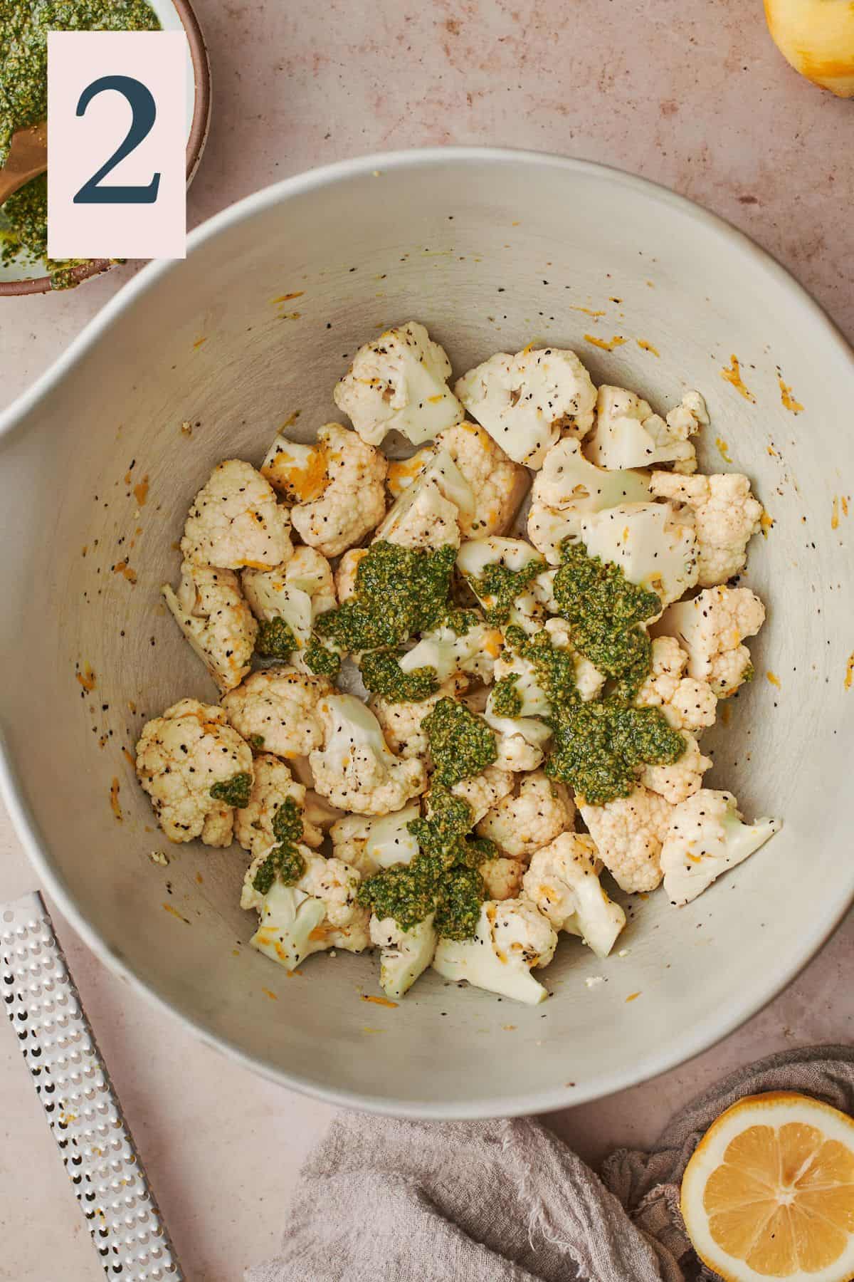 cauliflower florets in a large mixing bowl with pesto drizzled over the top.
