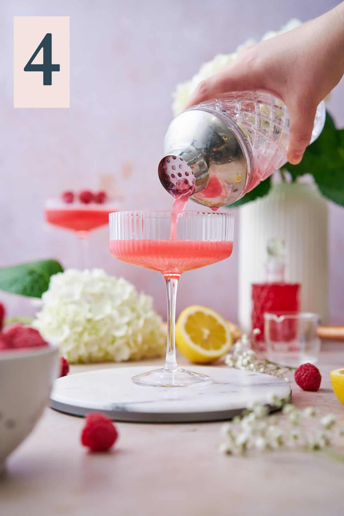 pouring pink raspberry martinis into coupe glasses from a cocktail shaker.