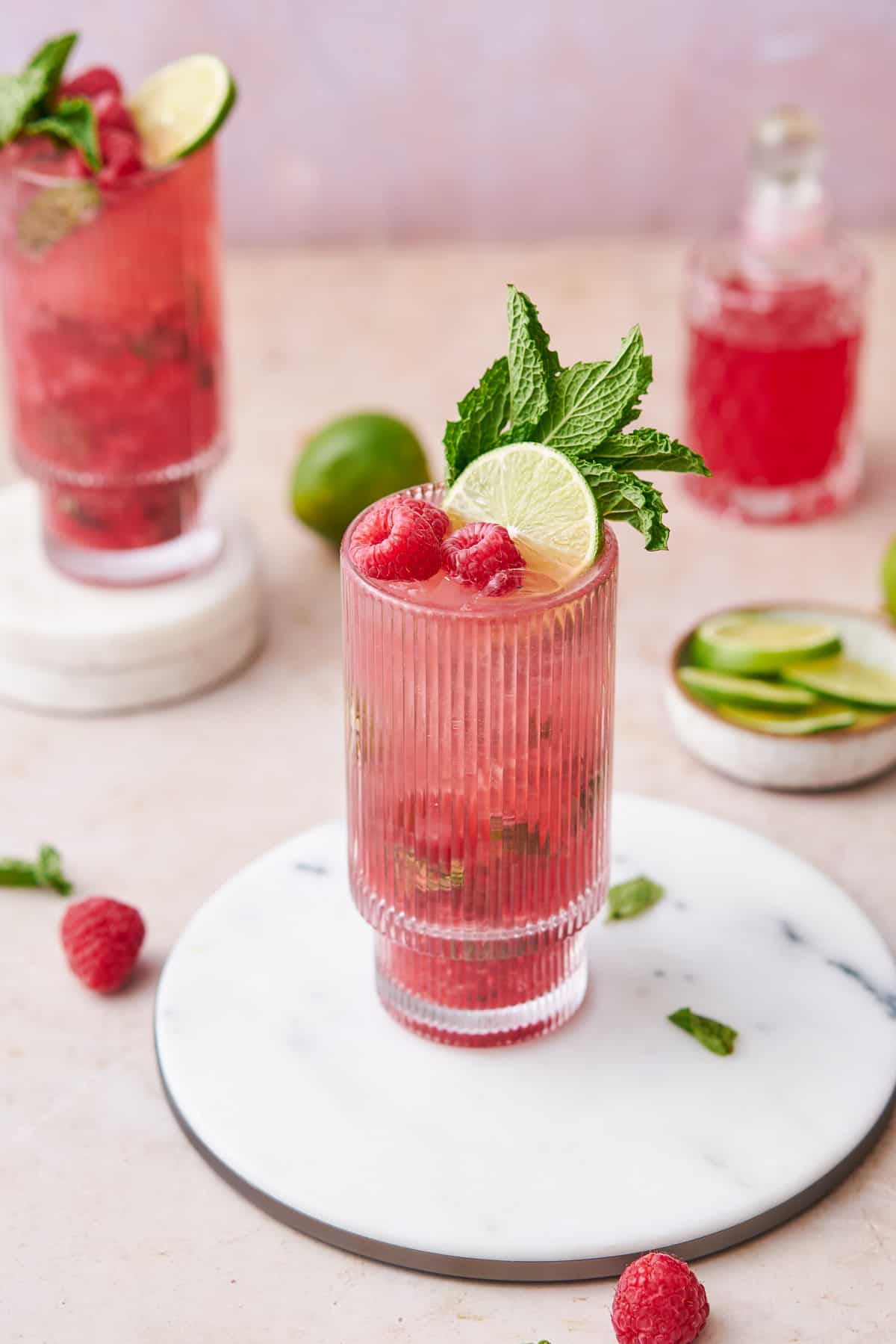 raspberry mojito shot 45 degrees, garnished with raspberry, limes, and mint.