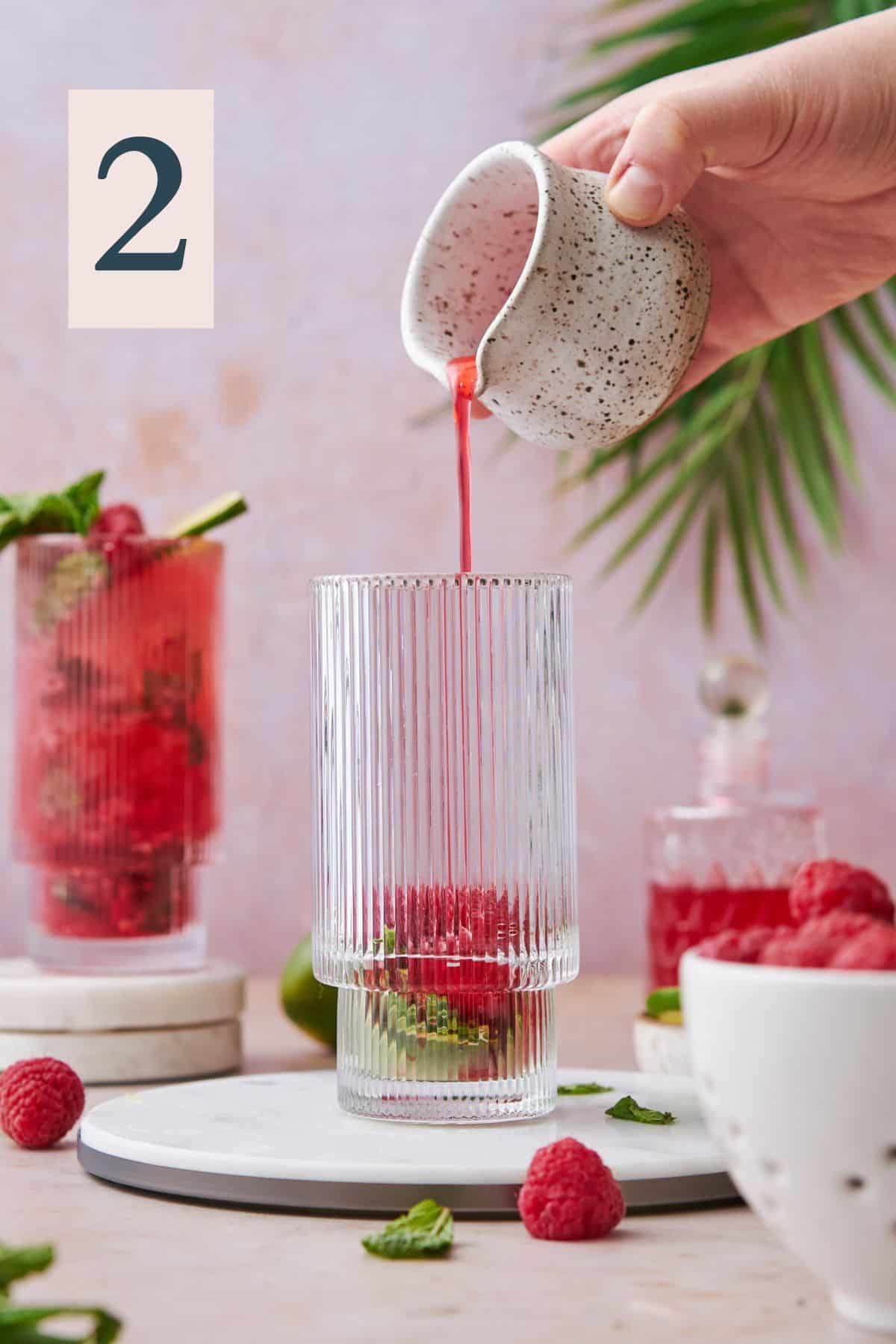 Adding raspberry simple syrup to a glass with mint and raspberry.