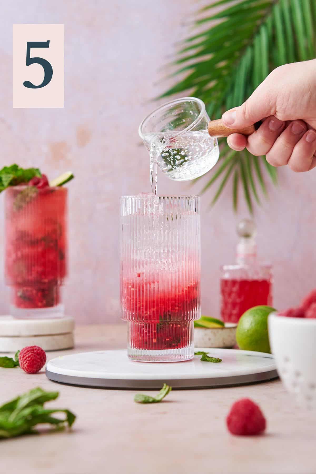 Topping raspberry mojito off with club soda with a shot pourer.