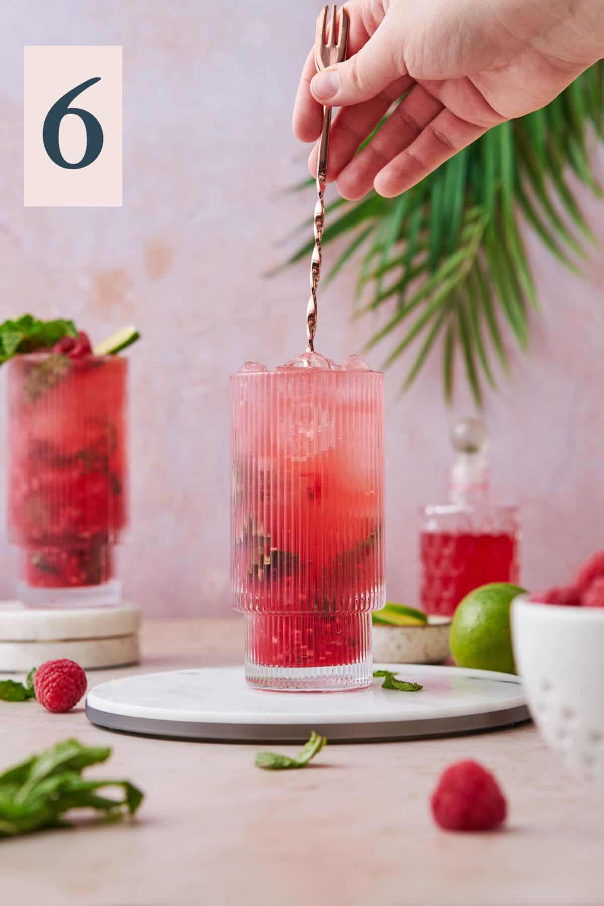Stirring raspberry mojito to mix ingredients together to finish off the drink.