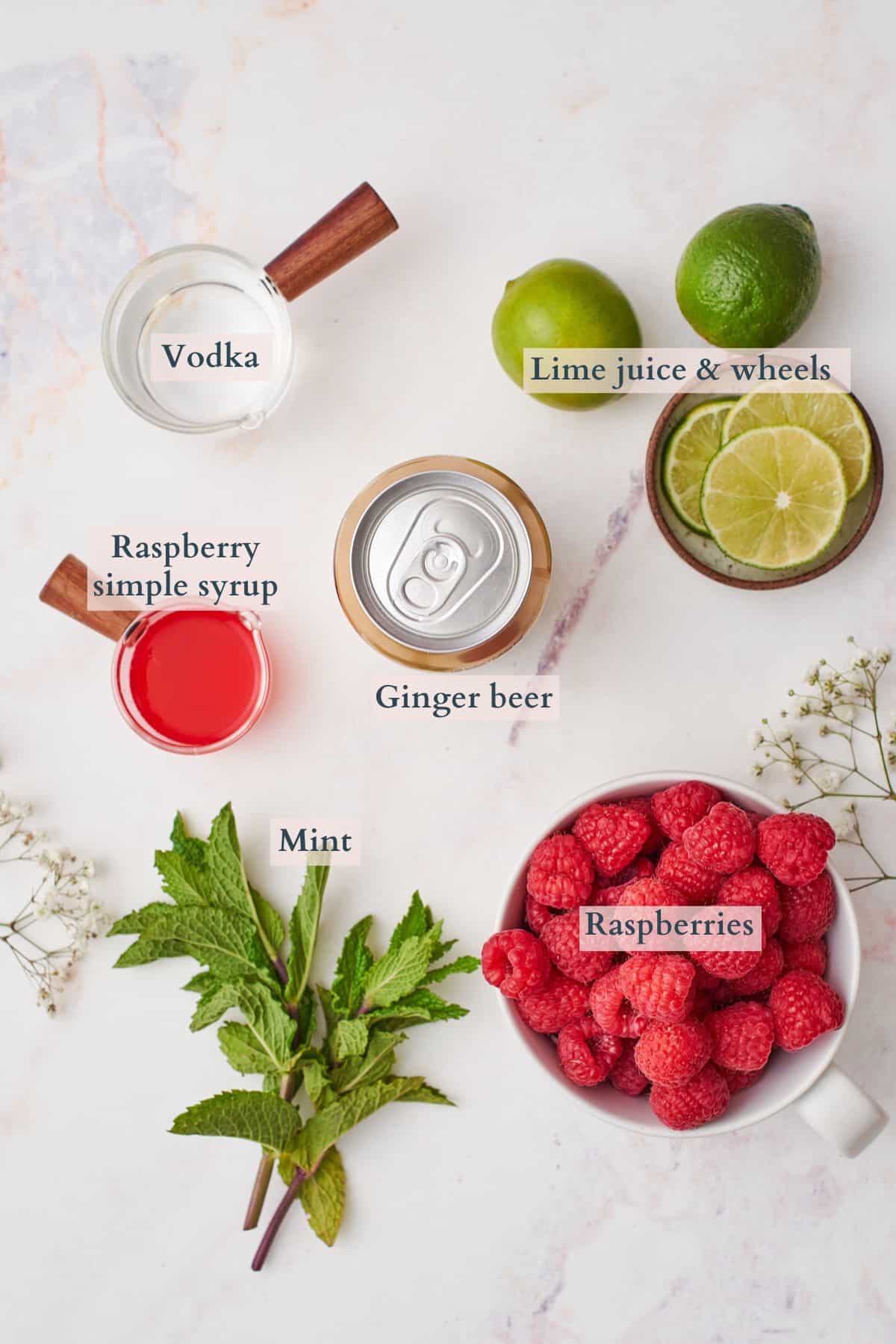 ingredients to make a raspberry mule laid out in small bowls with text overlaying to denote each ingredient. 