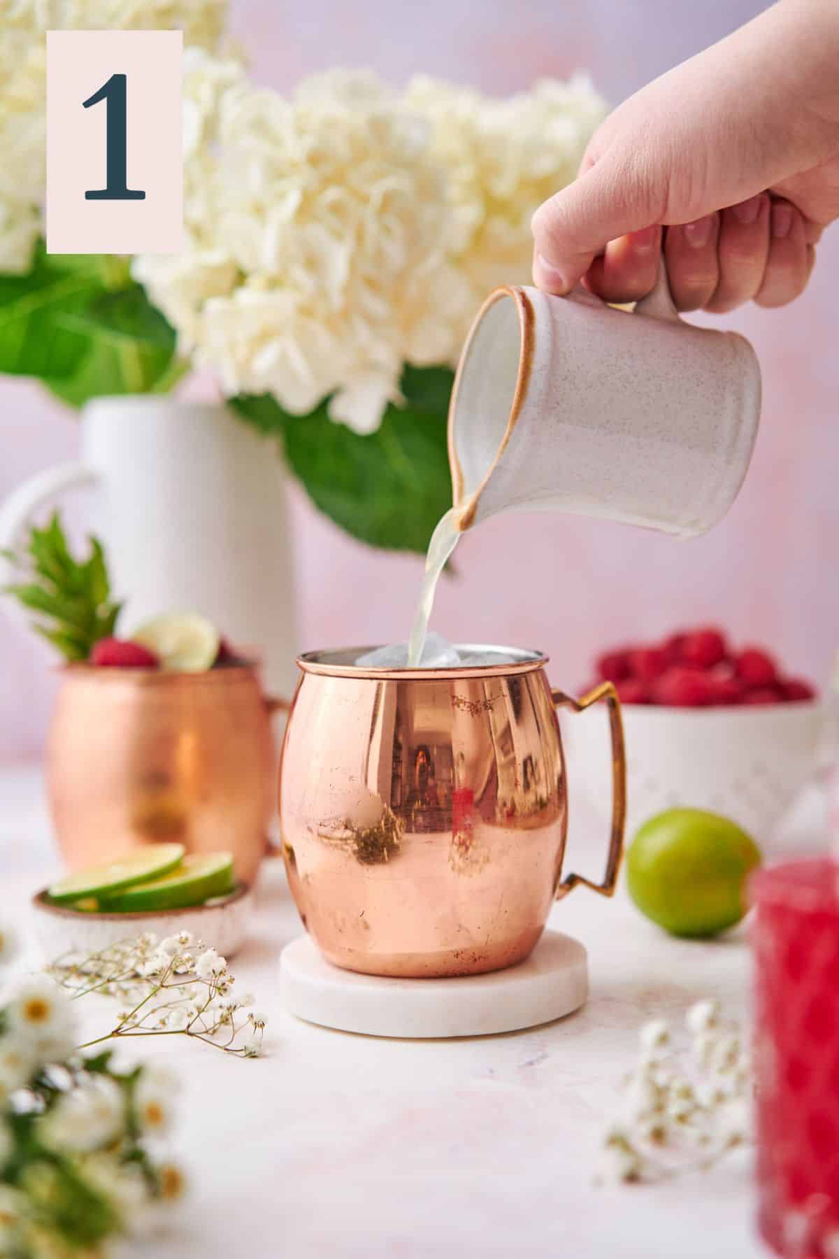 hand pouring lime juice into a copper moscow mule mug with fresh raspberries, hydrangeas, and other small white flowers.  