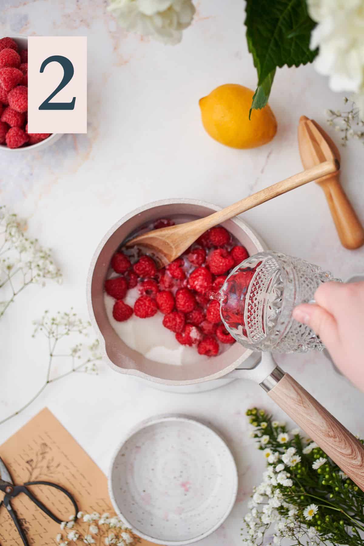 hand pouring water into a small saucepan with raspberries and sugar.