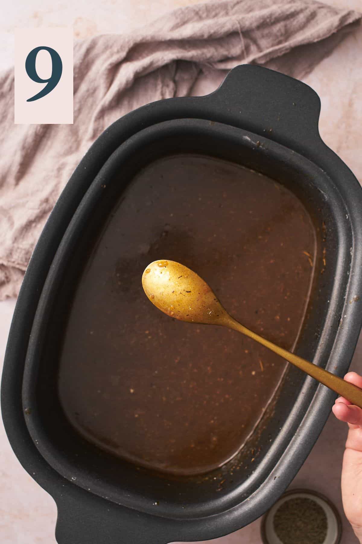 gravy in a slow cooker with a spoon held up to the camera with gravy coating the back of a spoon. 