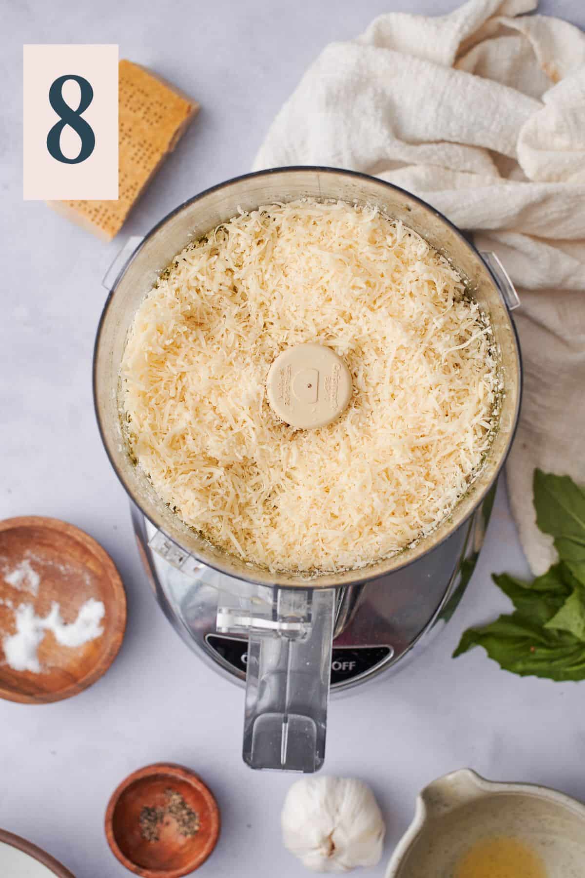 Adding grated parmesan to food processor to add finishing touch to walnut pesto.