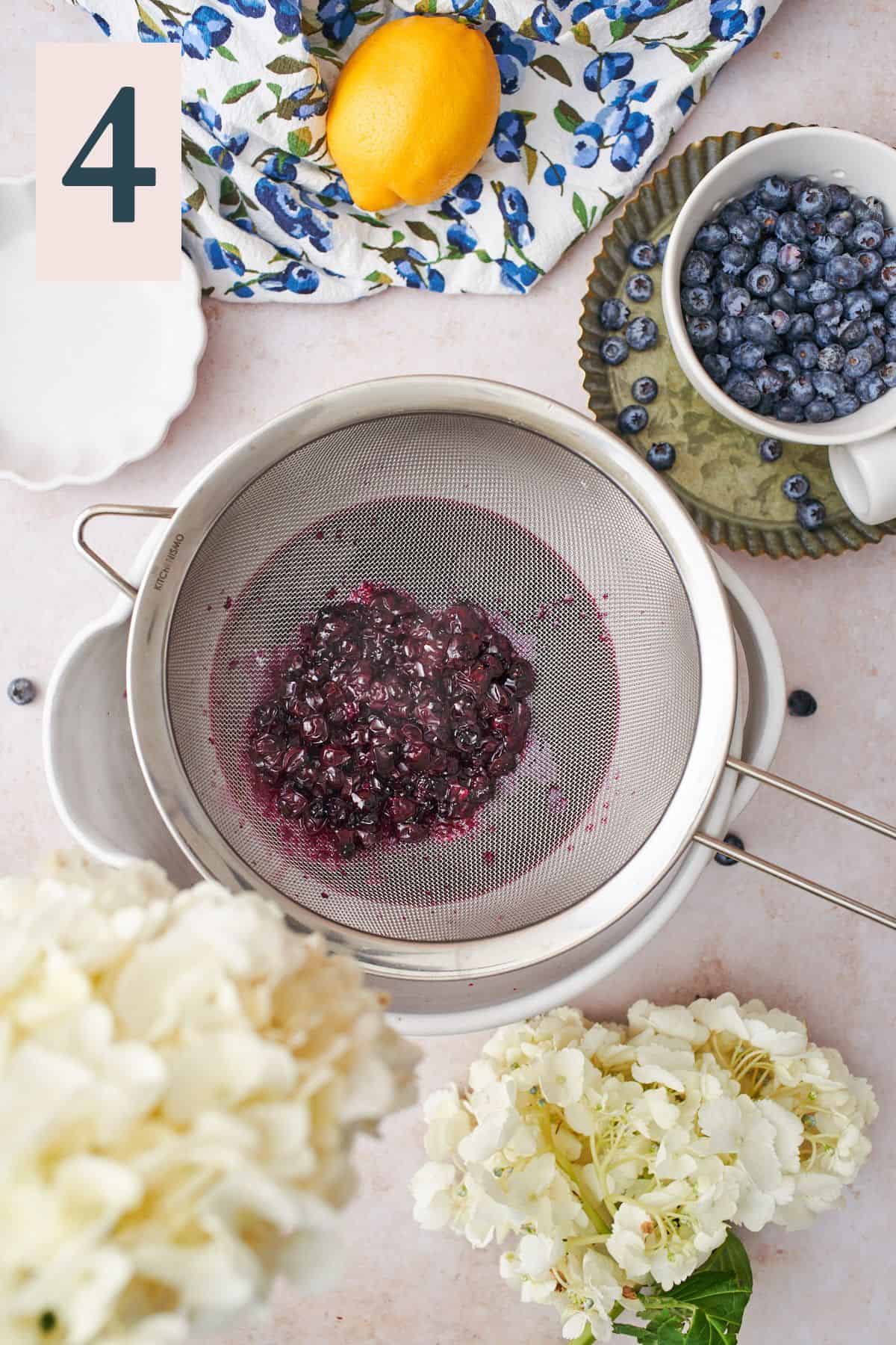 cooked blueberries being strained through a metal sieve into a bowl. 