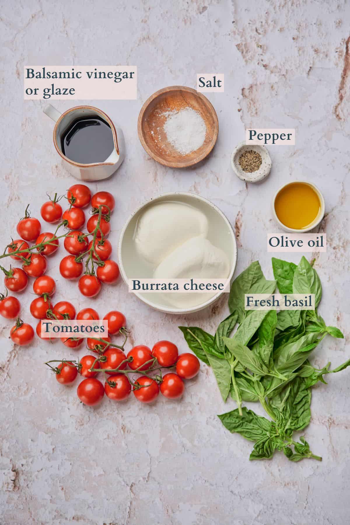 Burrata caprese salad ingredients laid out in various bowls and fresh ingredients on a backdrop.