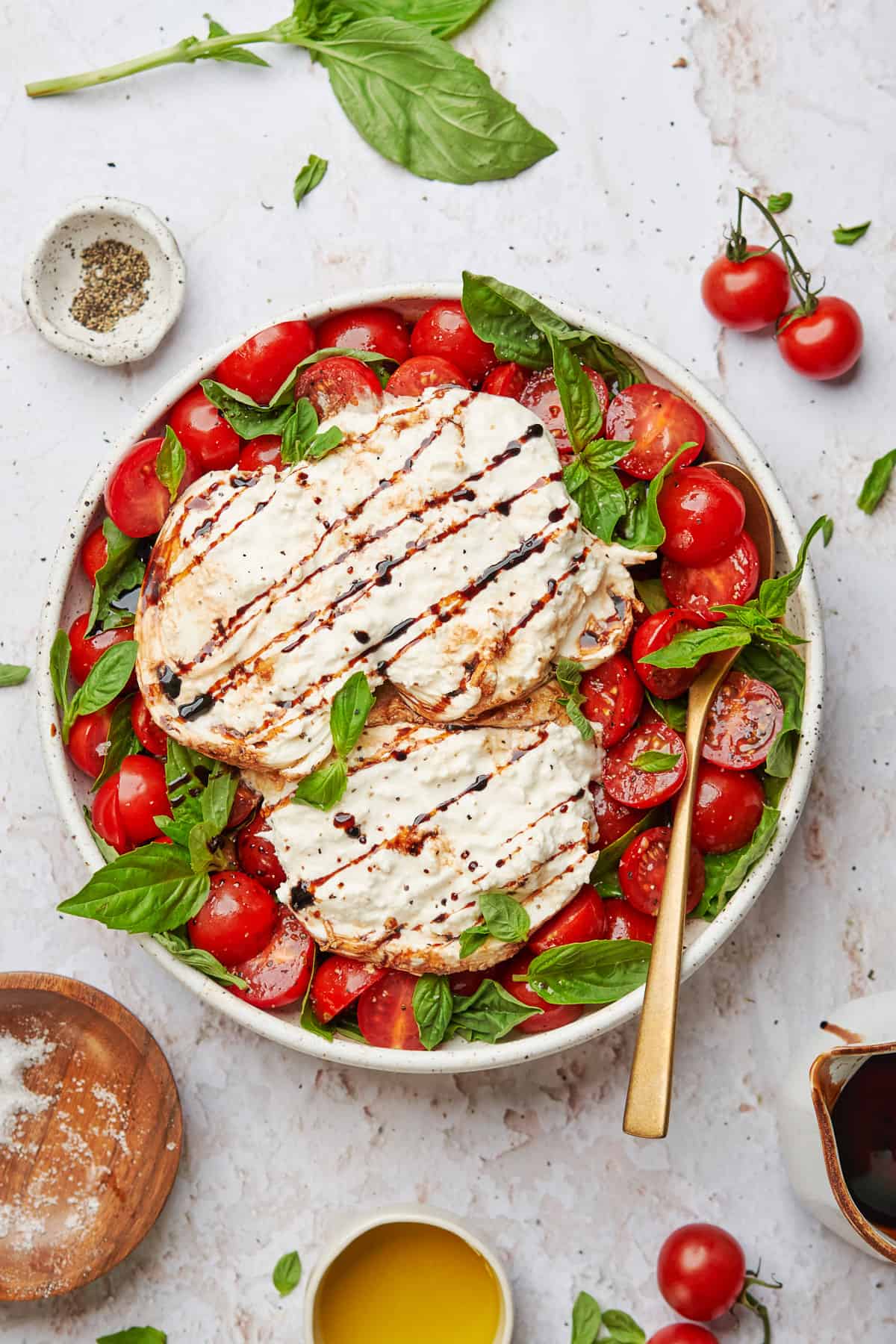 Burrata caprese salad with a basalmic reduction on top and surrounded by various ingredients.