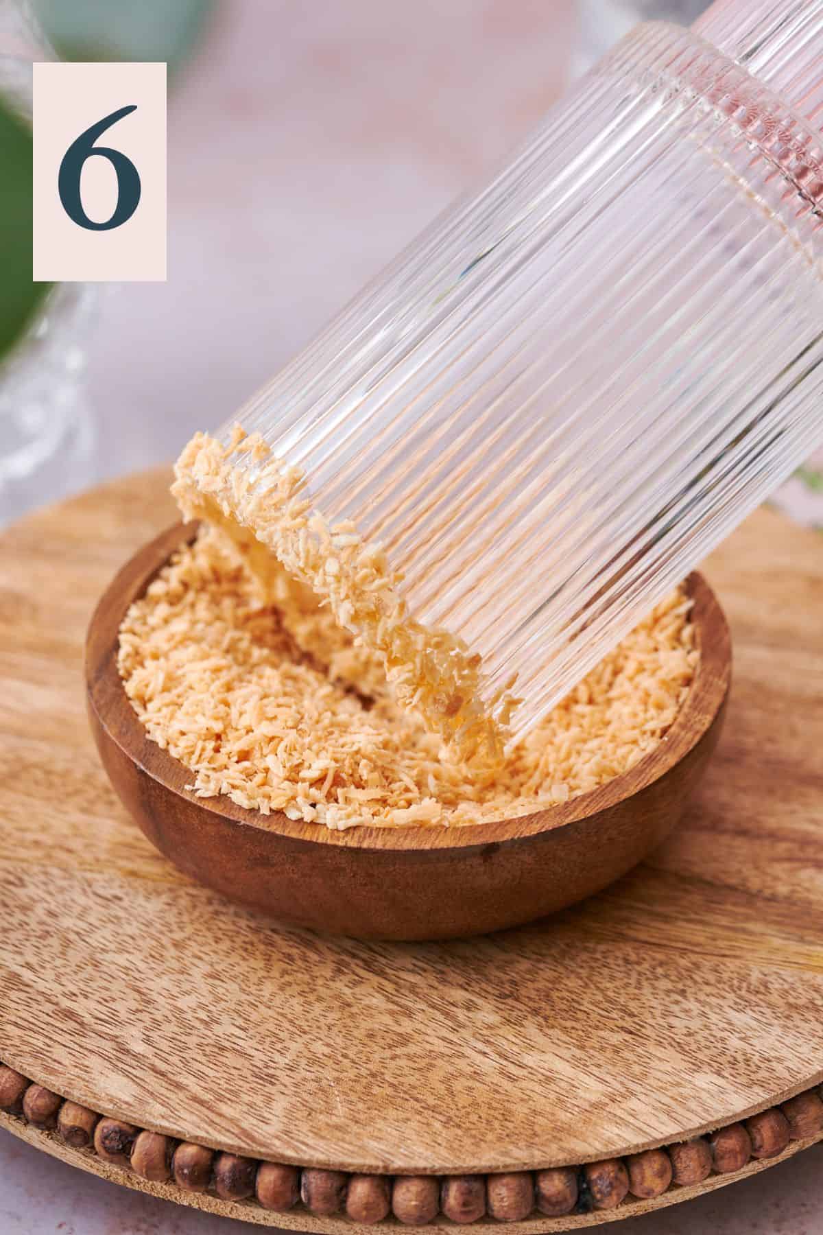 pressing a glass with maple syrup around the rim into a bowl of toasted coconut to get the flakes to stick to the edge of the glass.