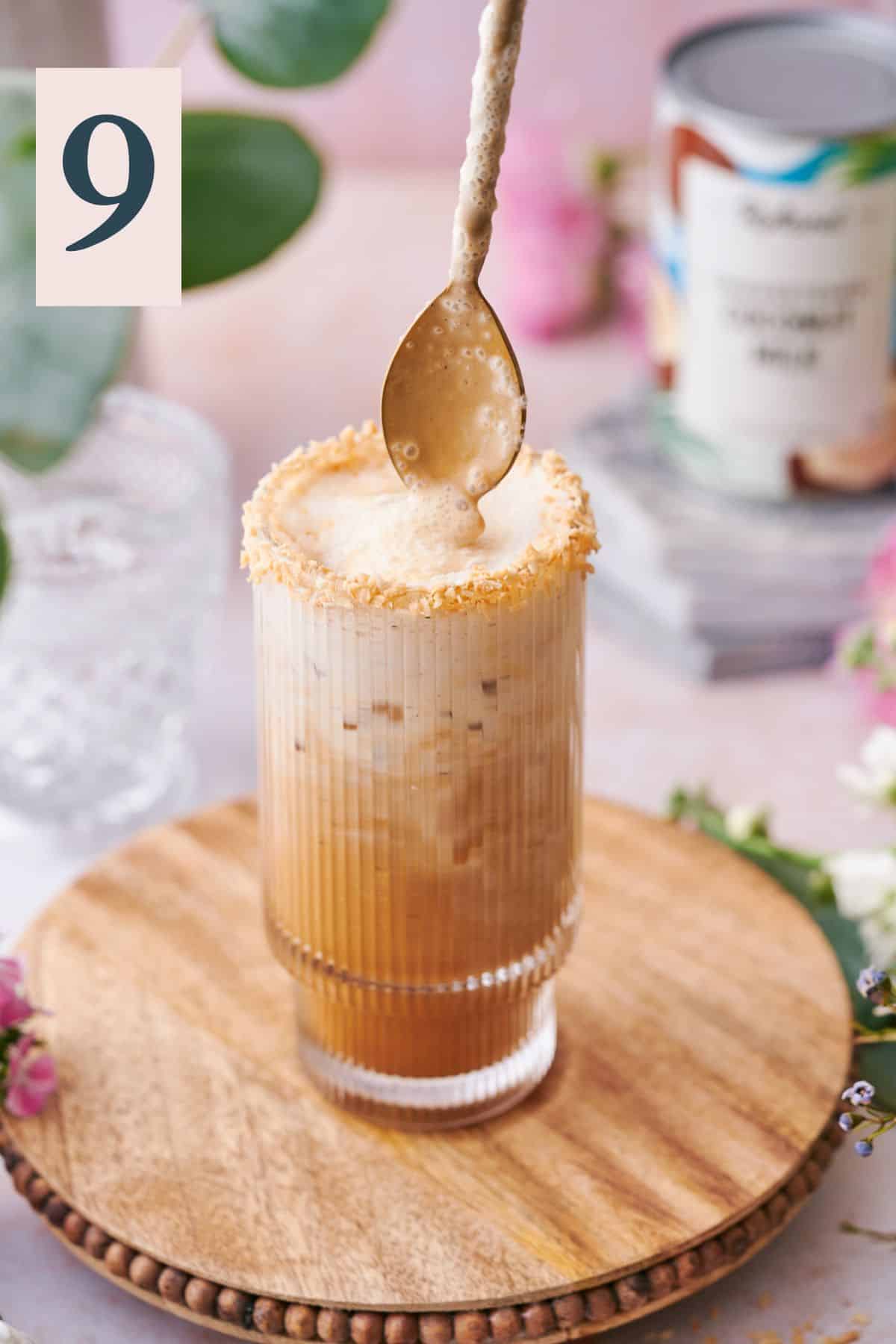 iced coconut milk latte being stirred together in a coffee glass with a spoon. 