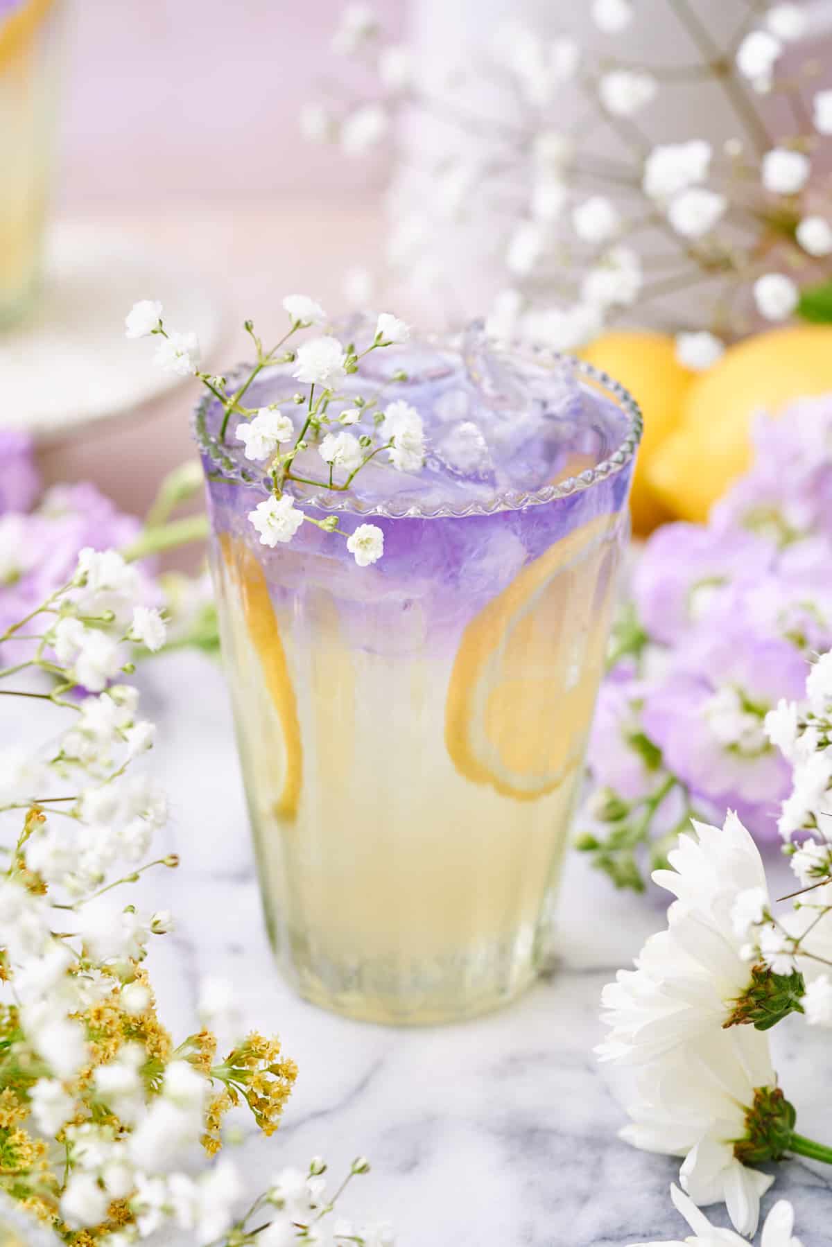 whimsical elderflower collins that is layered with a lemon yellow bottom and a purple empress gin top, topped with baby's breath flowers. 