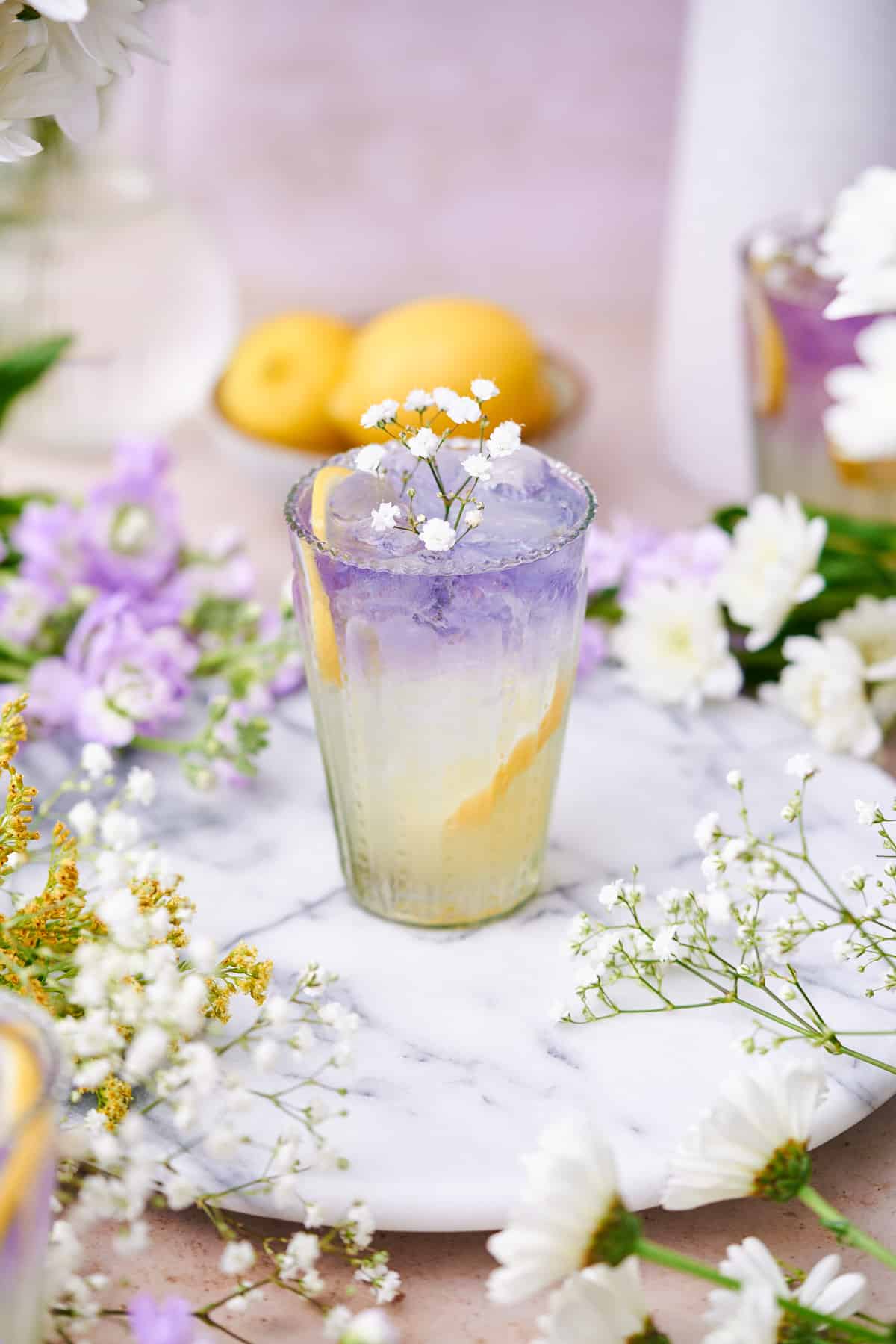 whimsical elderflower collins that is layered with a lemon yellow bottom and a purple empress gin top, topped with baby's breath flowers.