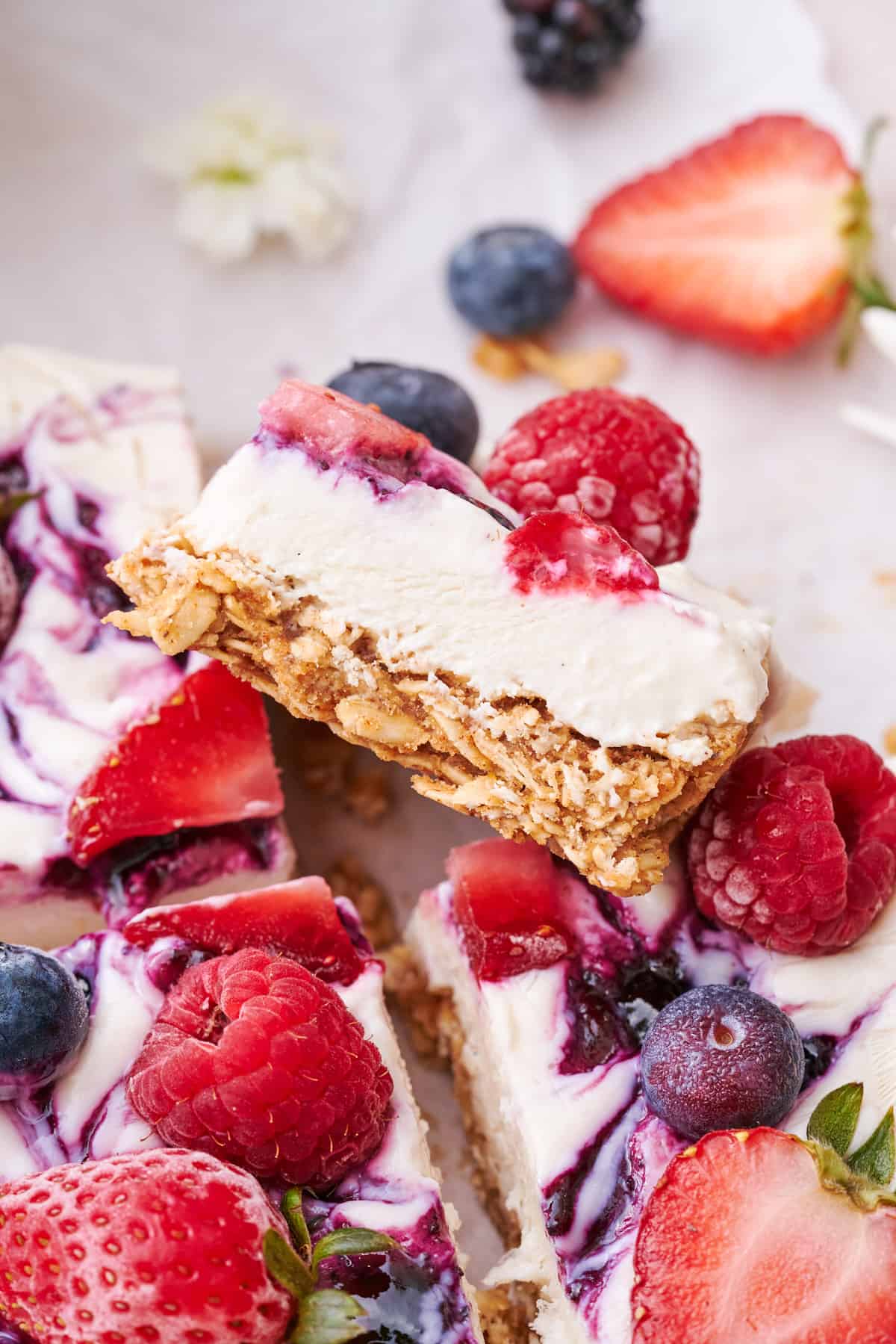 close up shot of a frozen yogurt and granola bar, with a cut bar facing the camera to show off the layers, and topped with blueberry jam and fresh mixed berries. 