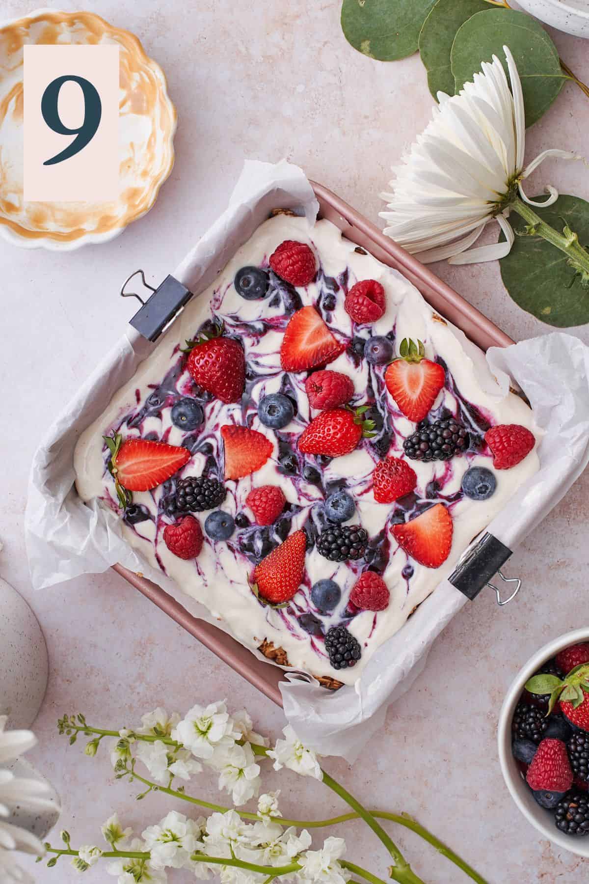 berries on top of a yogurt granola base in a baking dish with parchment paper. 