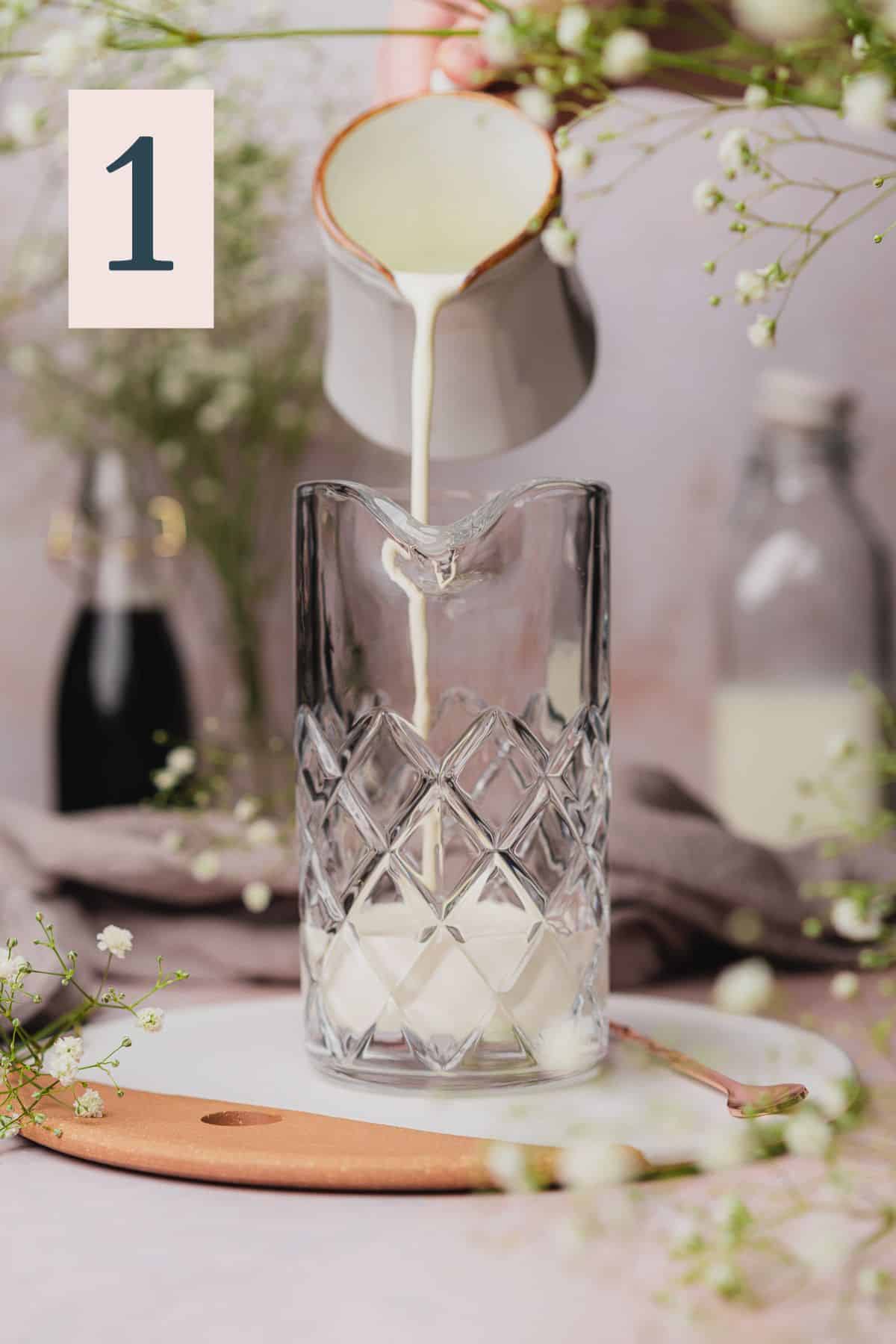 hand pouring heavy cream into a tall mixing jar, surrounded by baby's breath flowers. 