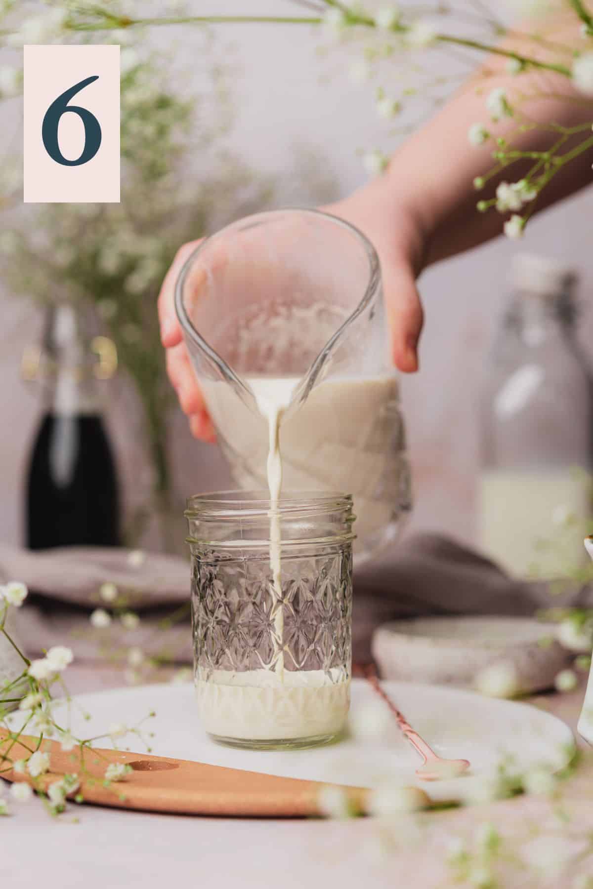 hand pouring sweet cream cold foam into a smaller jar. 