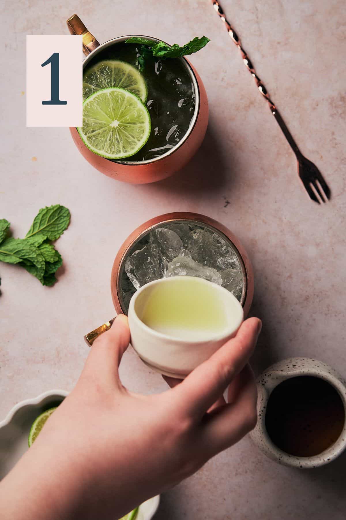 hand pouring fresh lime juice into an ice filled copper mug.