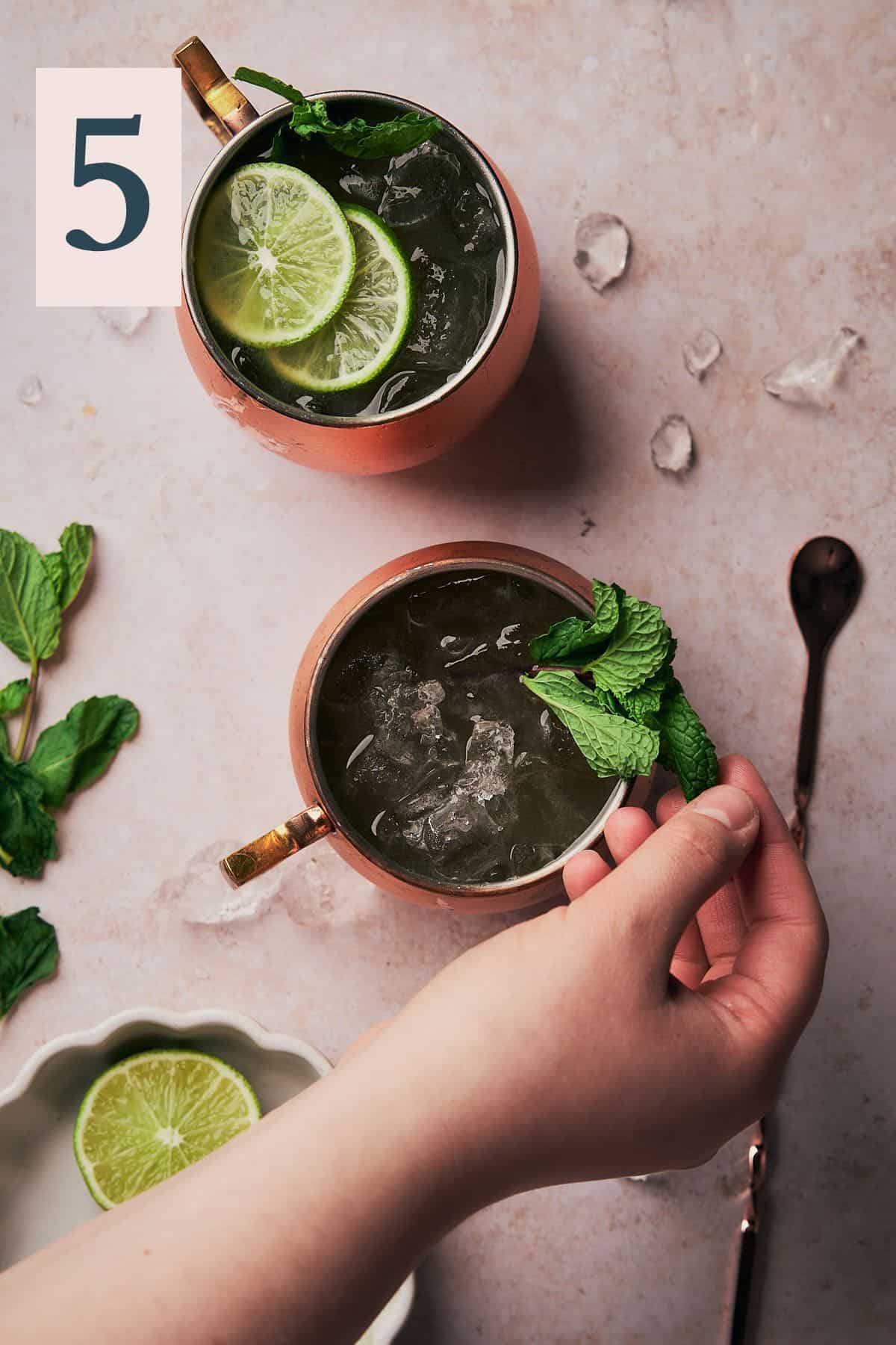 hand placing mint sprig into a copper mug.