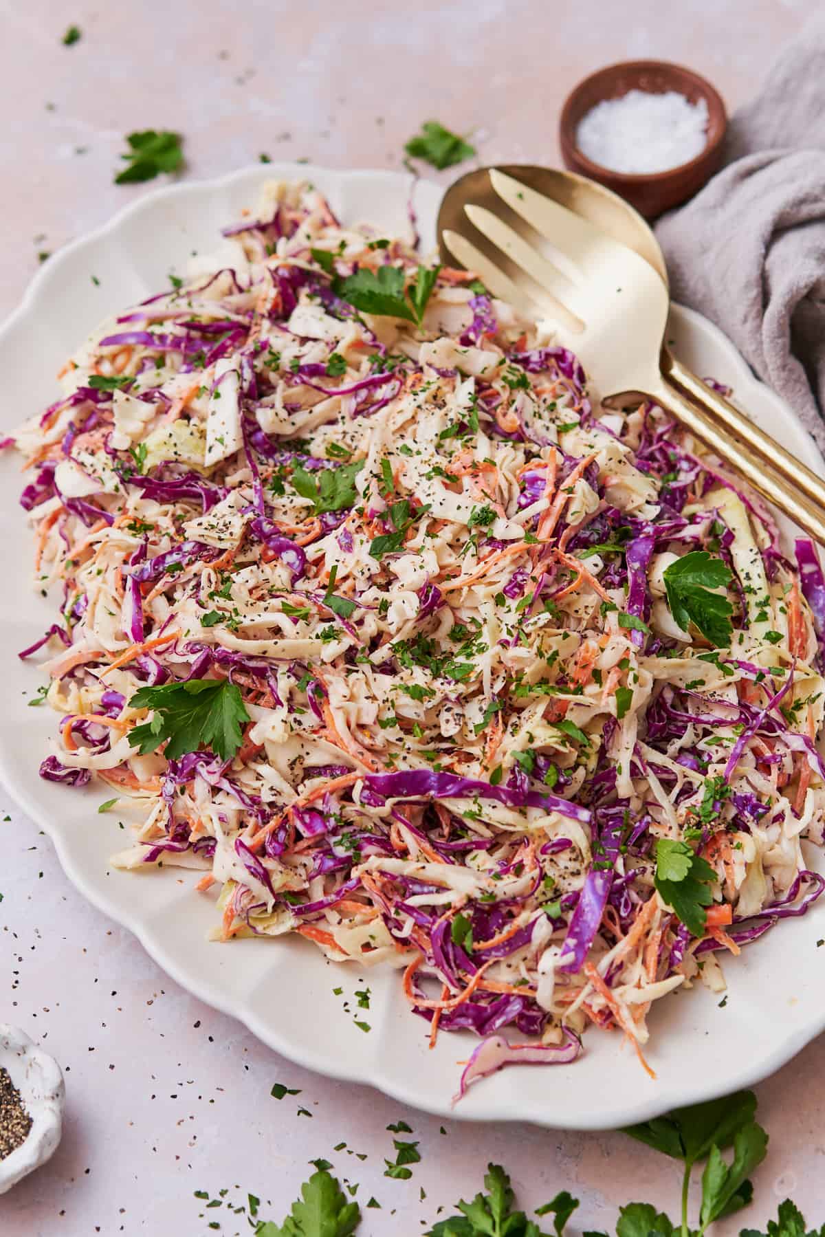 45 degree shot of coleslaw topped with parsley, salt and pepper on top of a large serving plate.