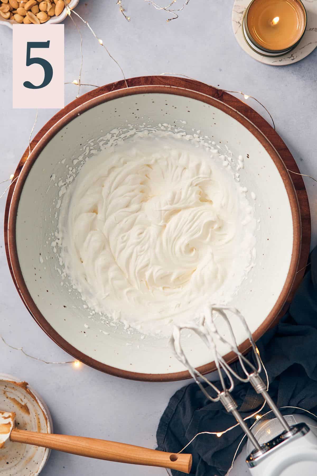 whipping heavy cream with an electric hand mixer in a large bowl.