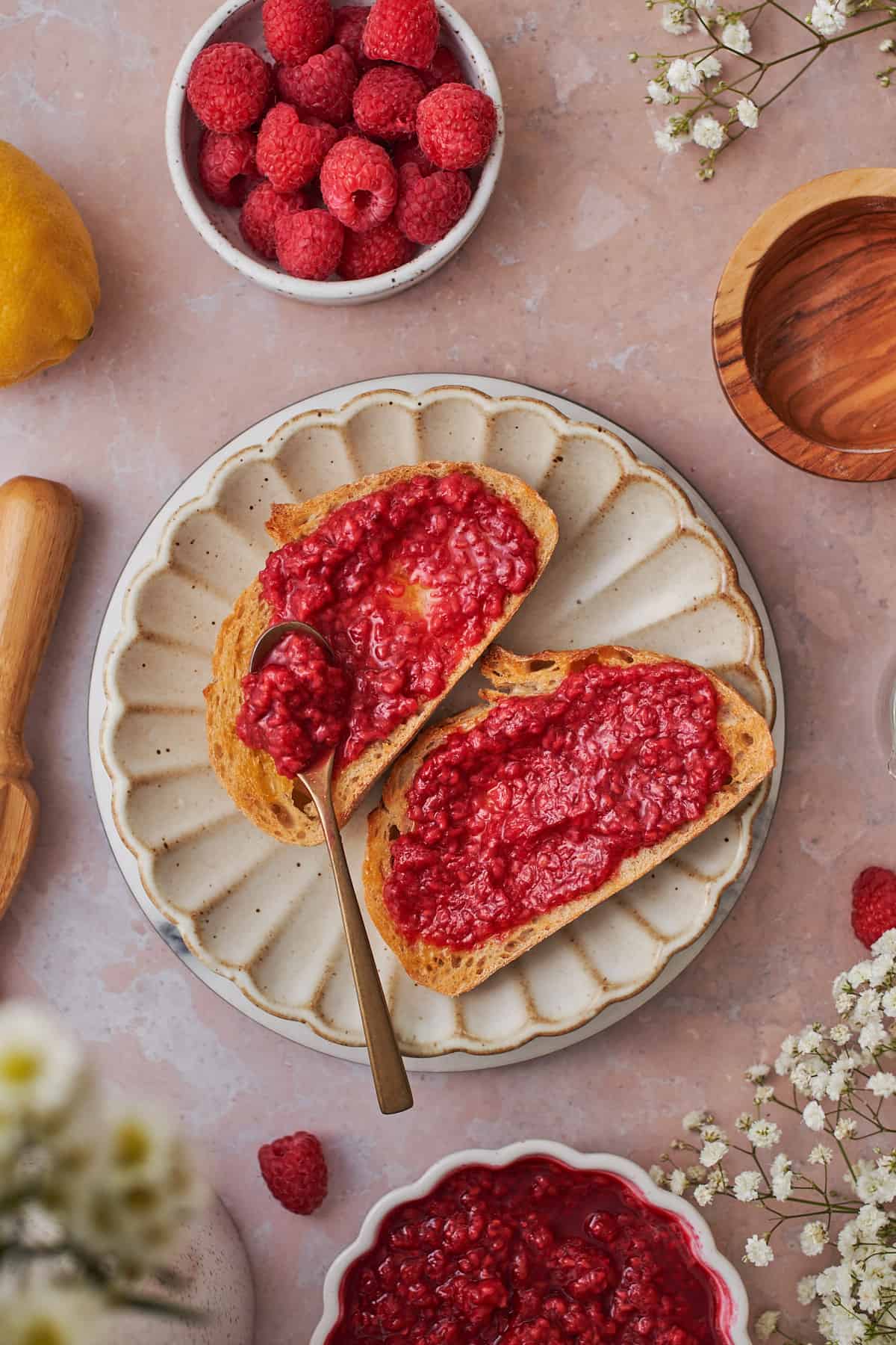 raspberry compote spread onto sourdough bread, with little white flowers surrounding the ruffled plate. 