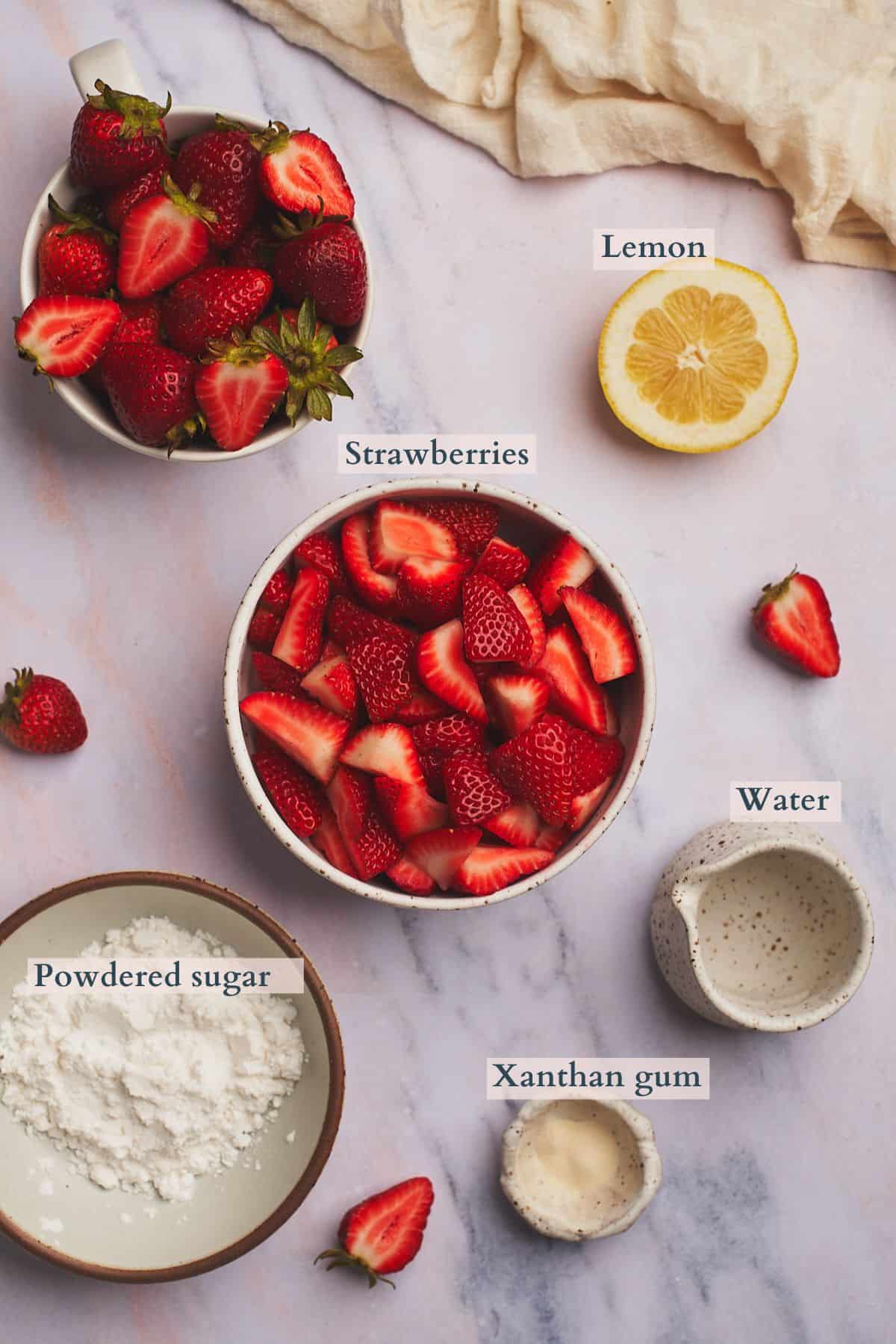 Strawberries, sugar, lemon juice, xanthan gum, and water laid out to make strawberry cheesecake topping, with labels to denote each ingredient. 