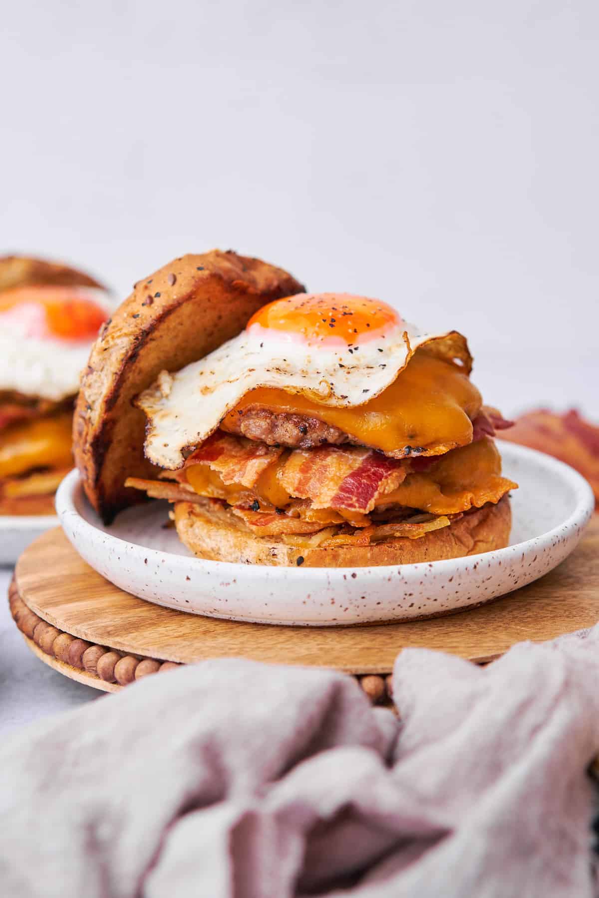 breakfast burger stacked high with crispy hash browns, bacon, burger patties, and fried sunny side up egg.