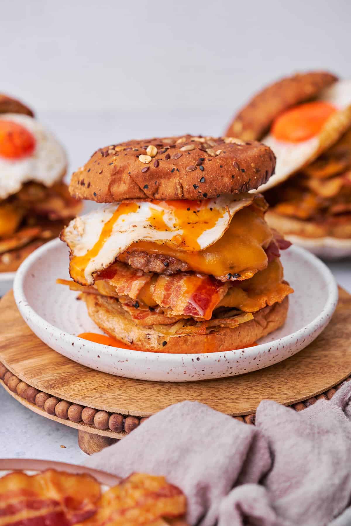 stacked breakfast burger on a seeded bun with a runny egg, bacon, patties, and hashbrowns. 