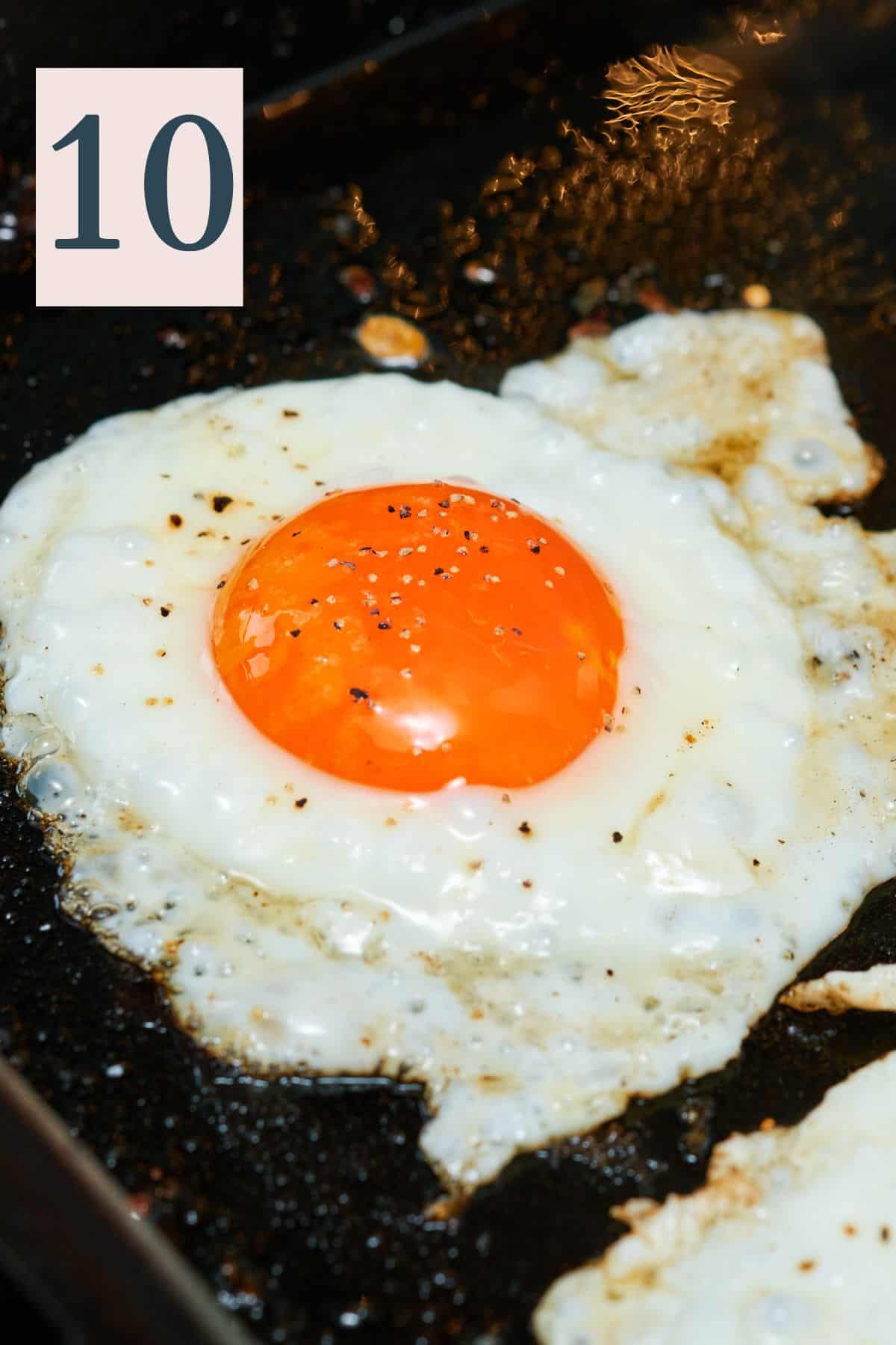 cooked sunny side up egg on a griddle with salt and pepper.
