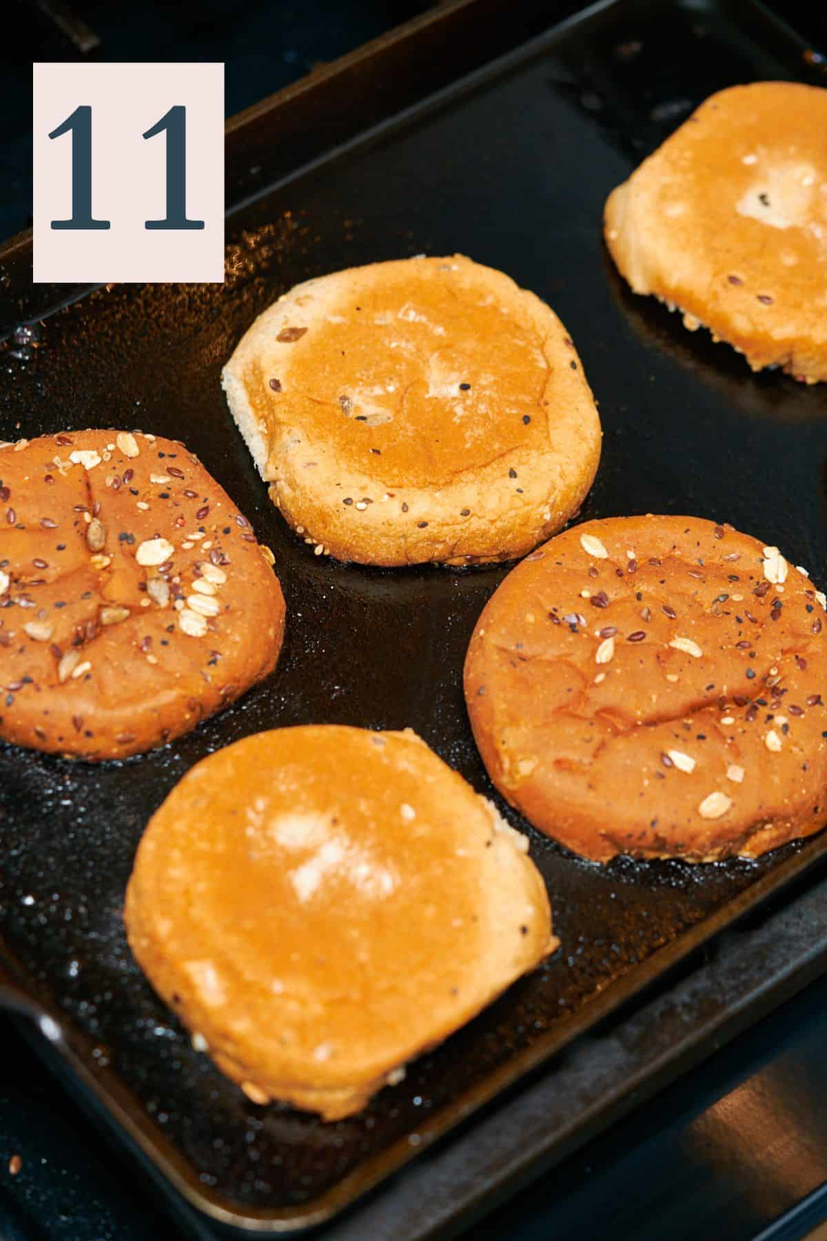 seeded buns face down on a griddle. 