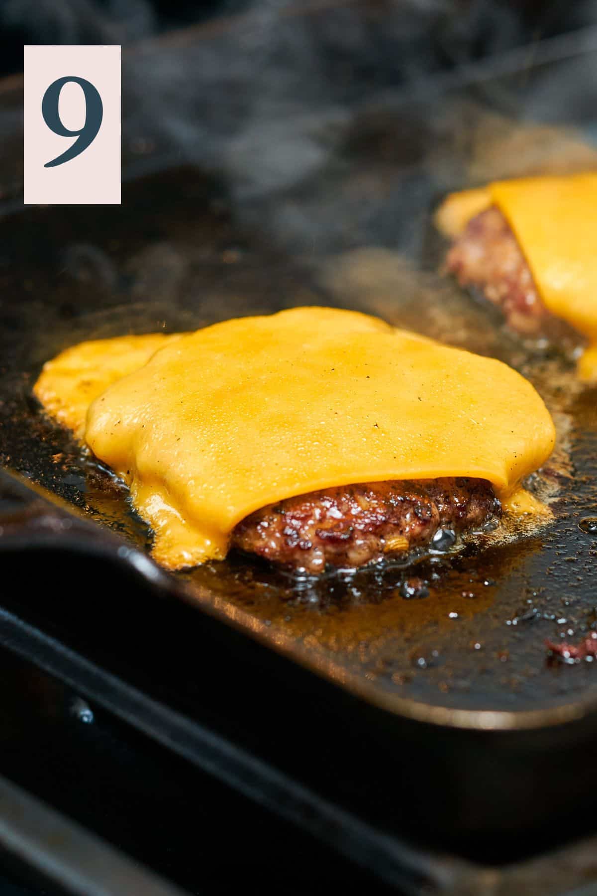 cooked burger patty with cheese melting on it on a hot griddle.