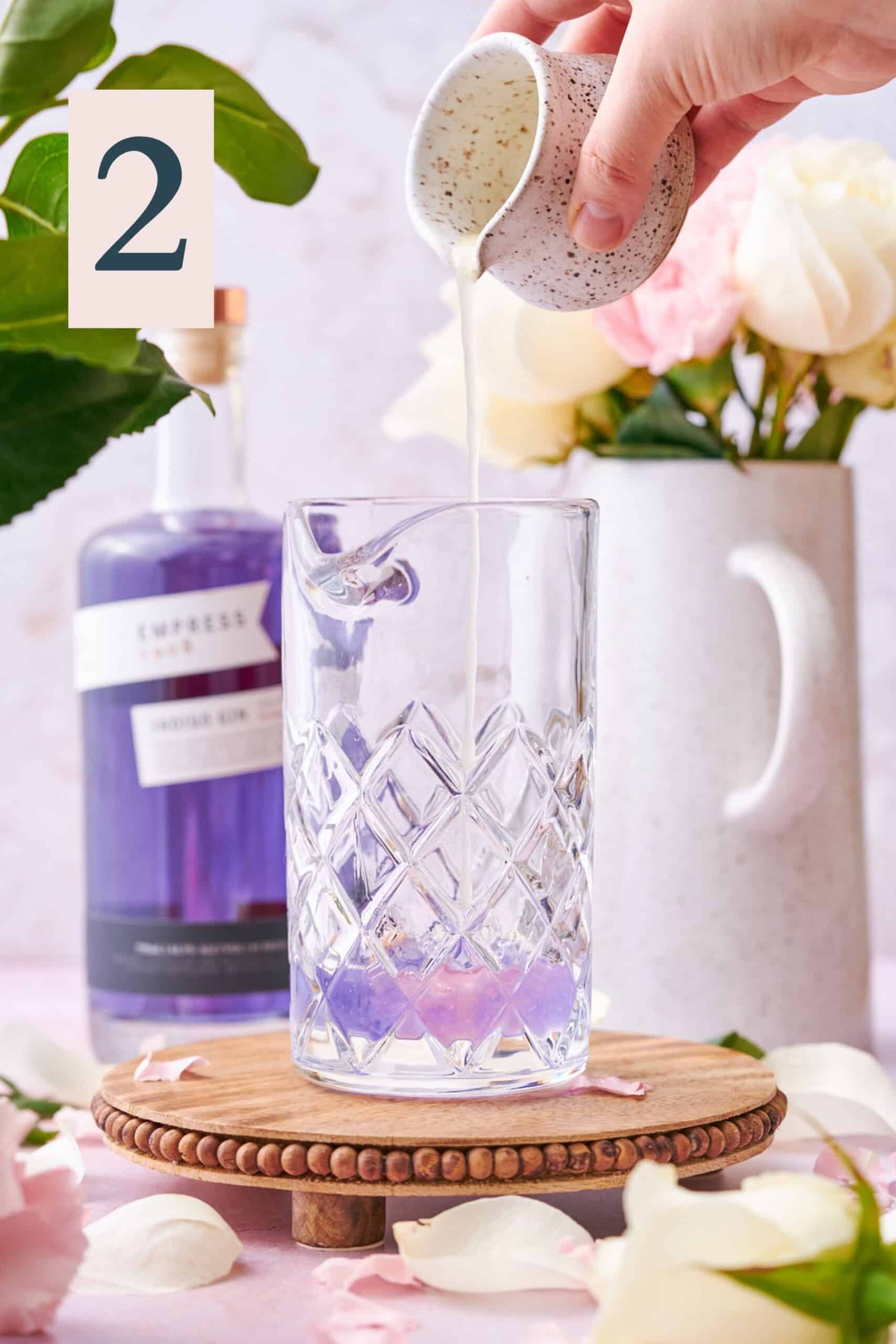 hand pouring lime juice into a mixing glass with empress gin, with the empress turning a pale pink color from purple. 