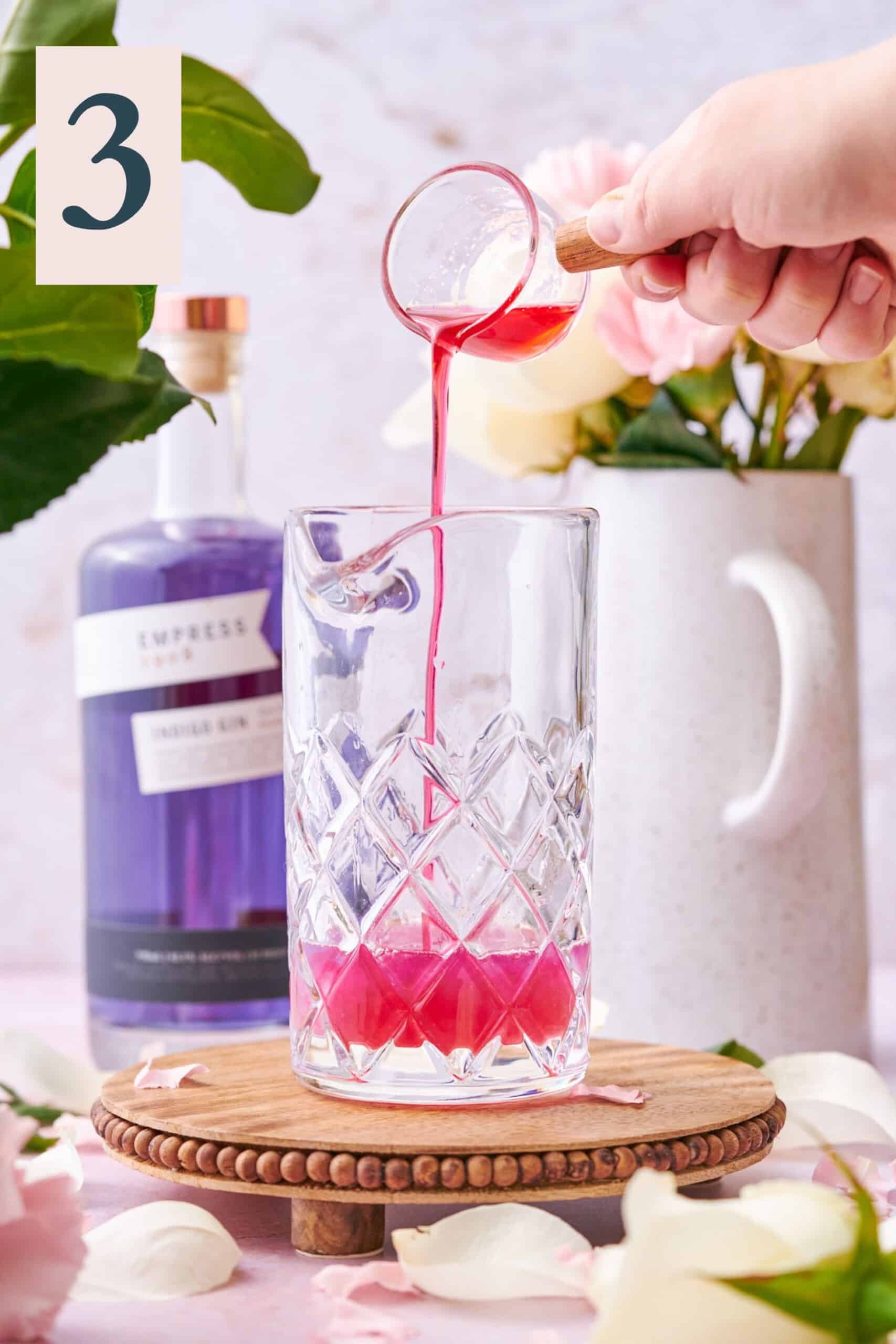 hand pouring raspberry syrup into a mixing glass. 