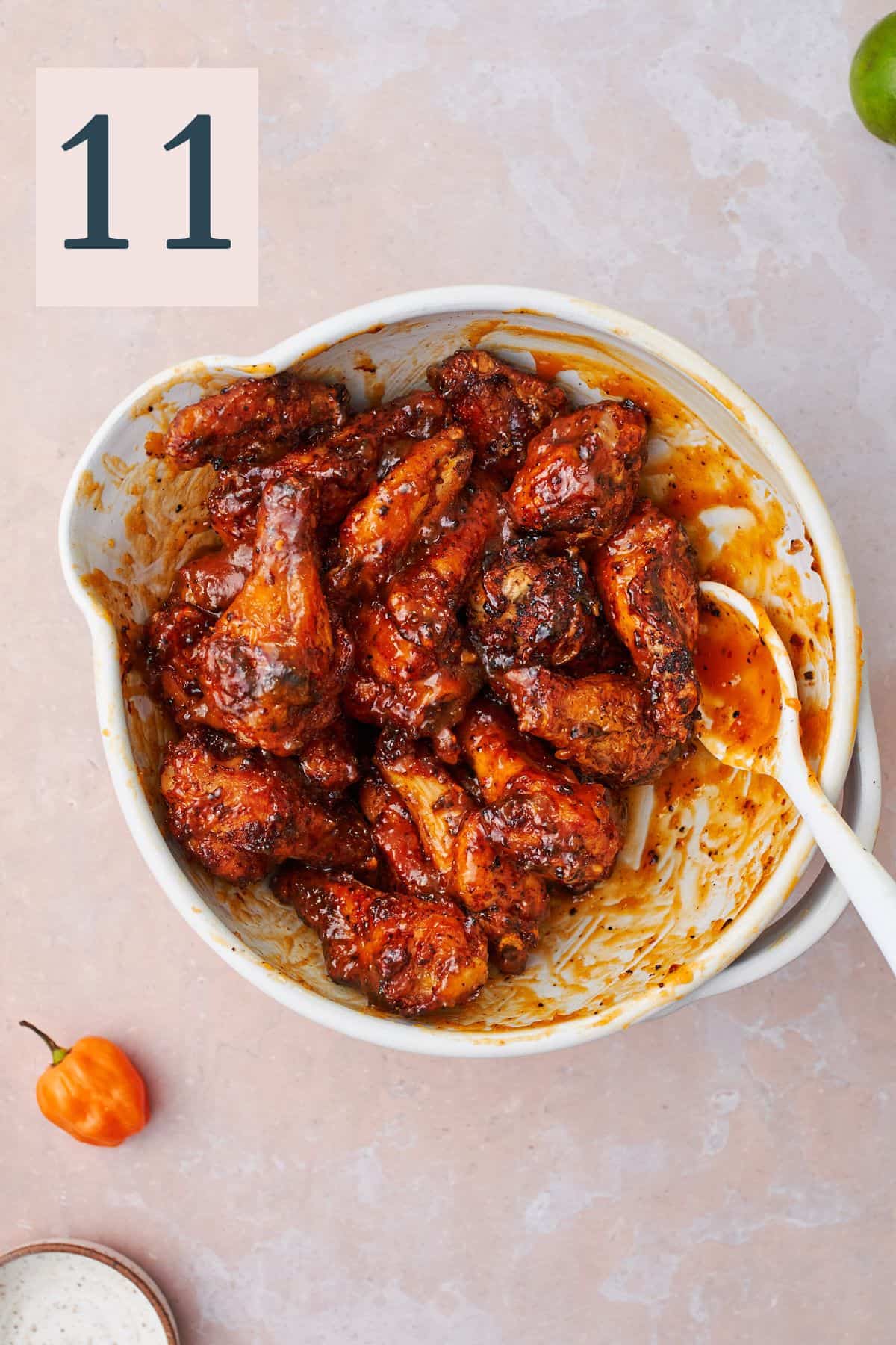 mango habanero sauce coating wings in a mixing bowl with a rubber spatula. 