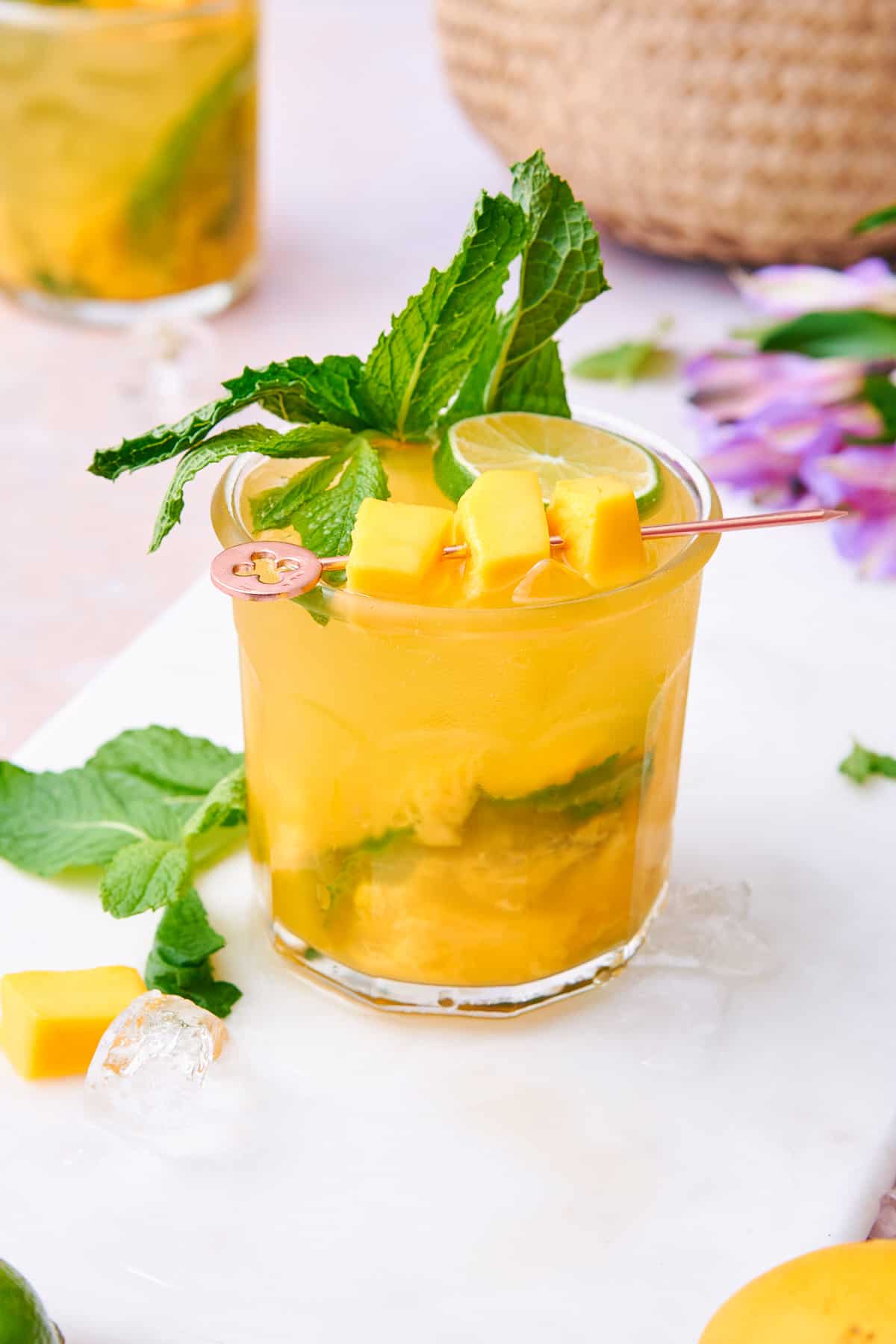 Garnishing the mango cocktail with mango chunks, lime slices, and mint leaves.
