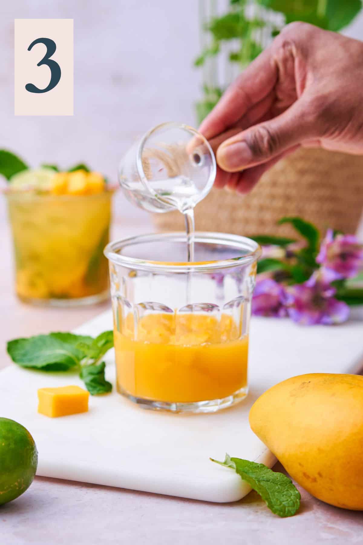 Pouring in simple syrup to mango cocktail mixture.